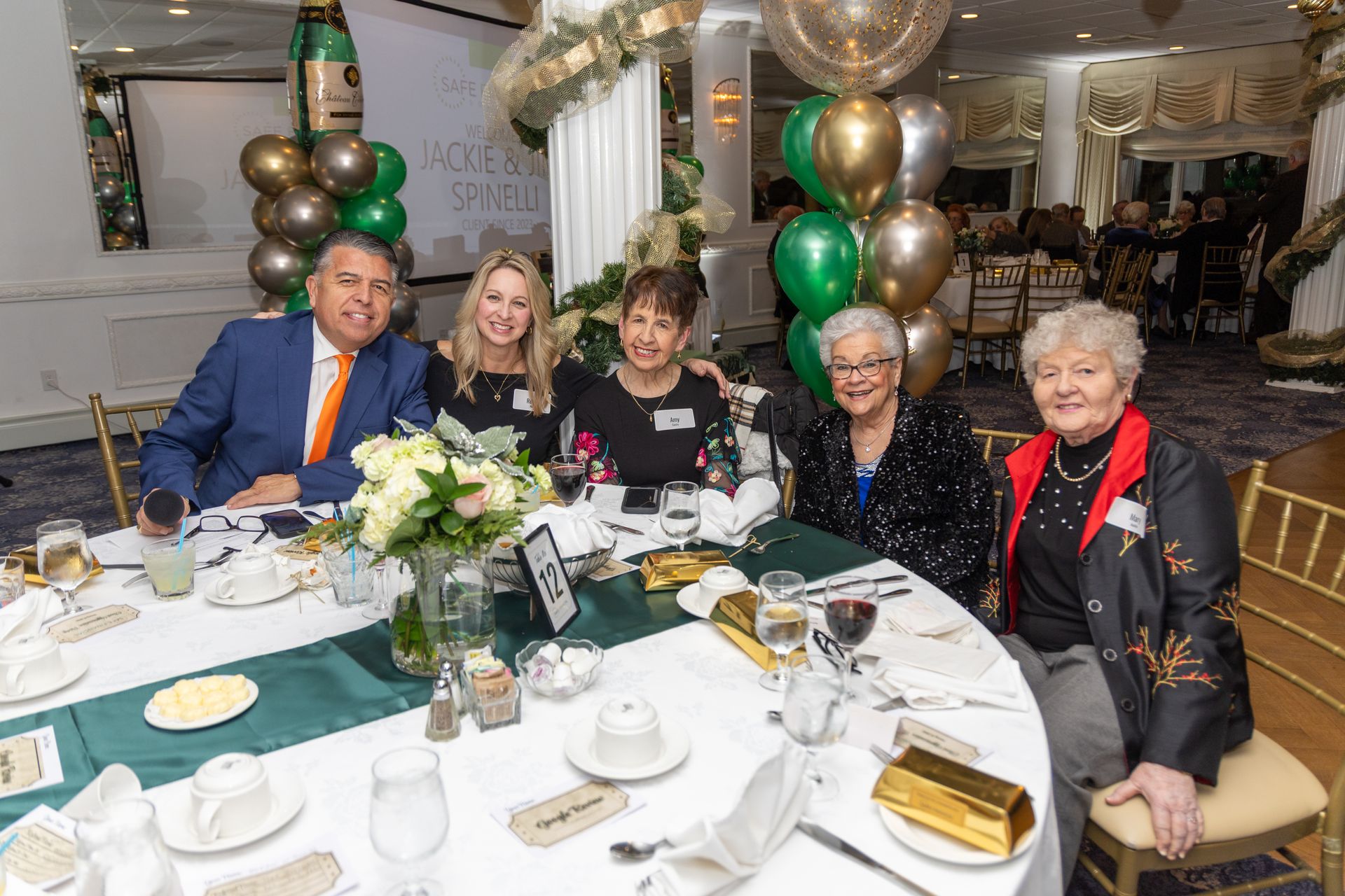 Group of people seated at a table at an event, with balloons and decorations.