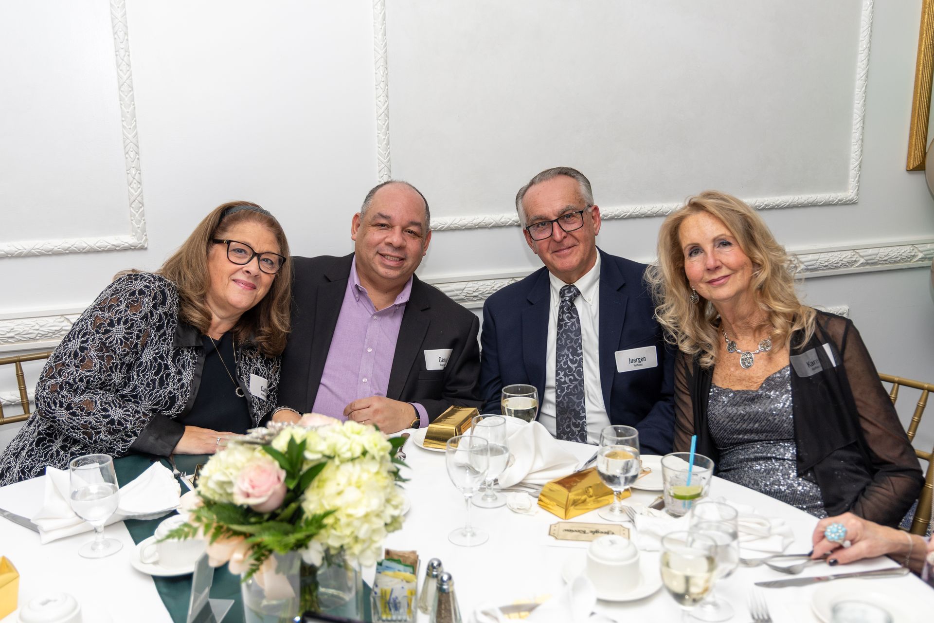Four people seated at a round table, smiling. Dinner setting with centerpiece.