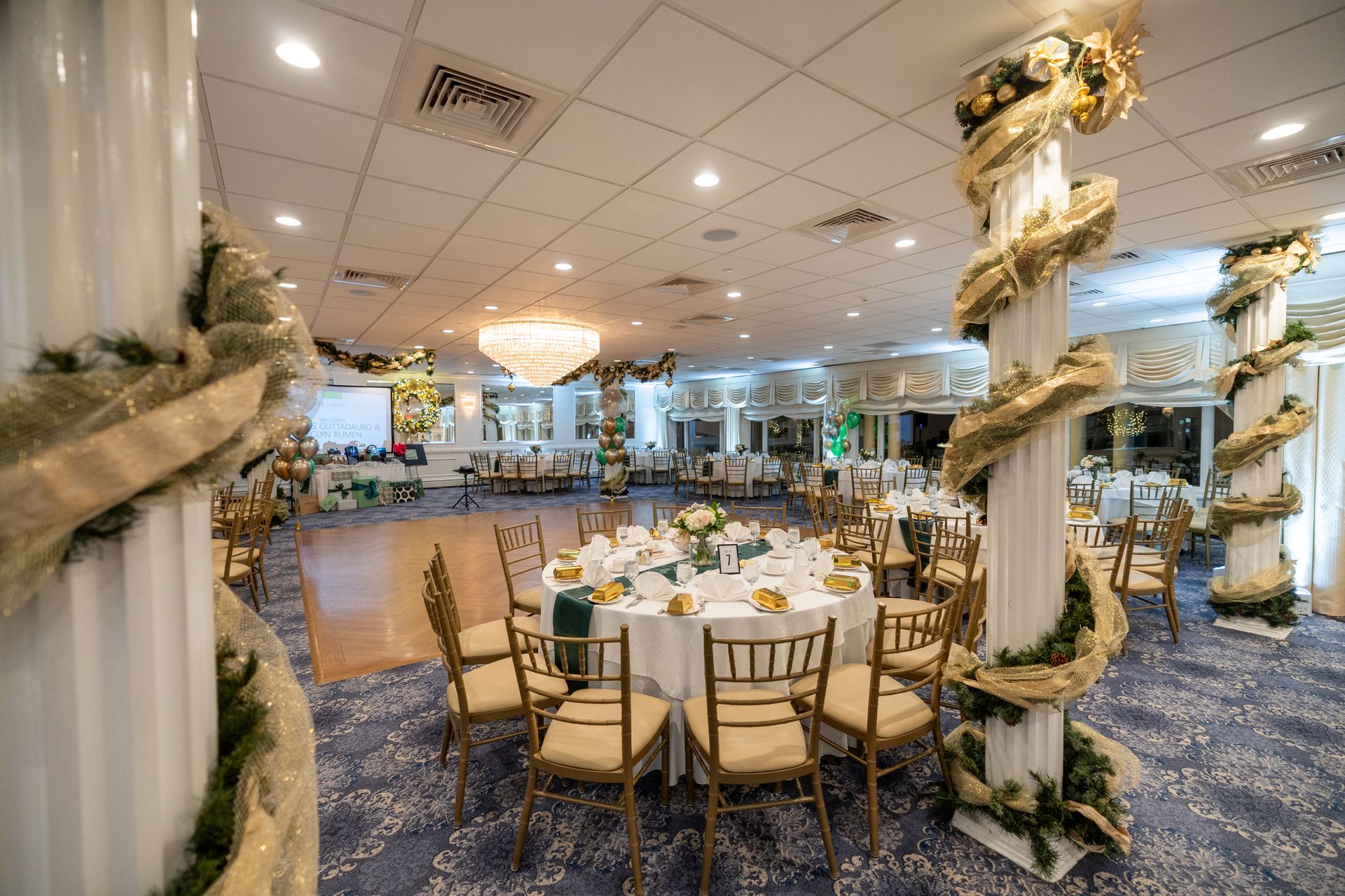 Banquet hall with round tables, decorated columns, and a dance floor.