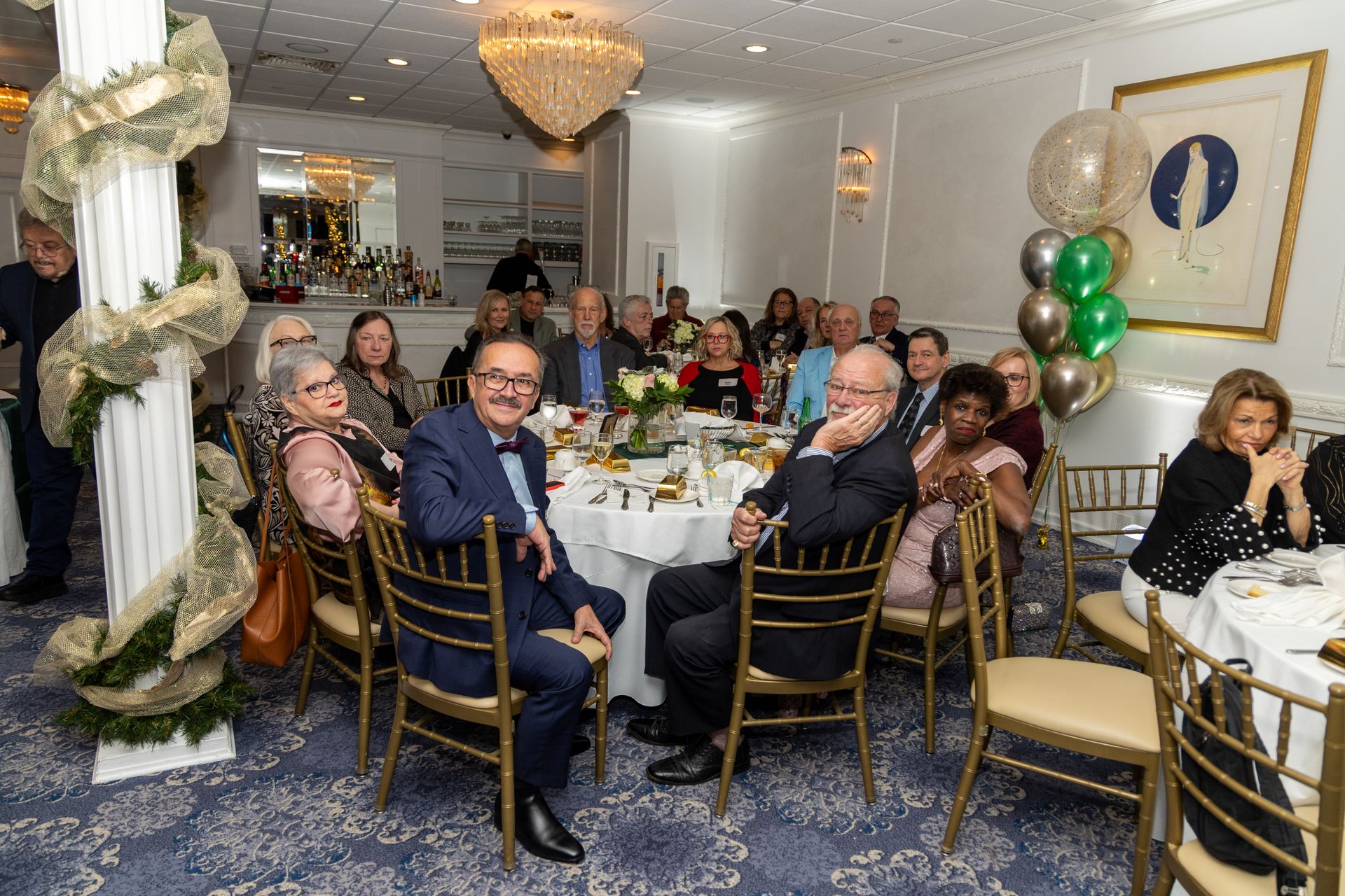 People seated at round tables in a decorated room, likely at a formal event or reception.