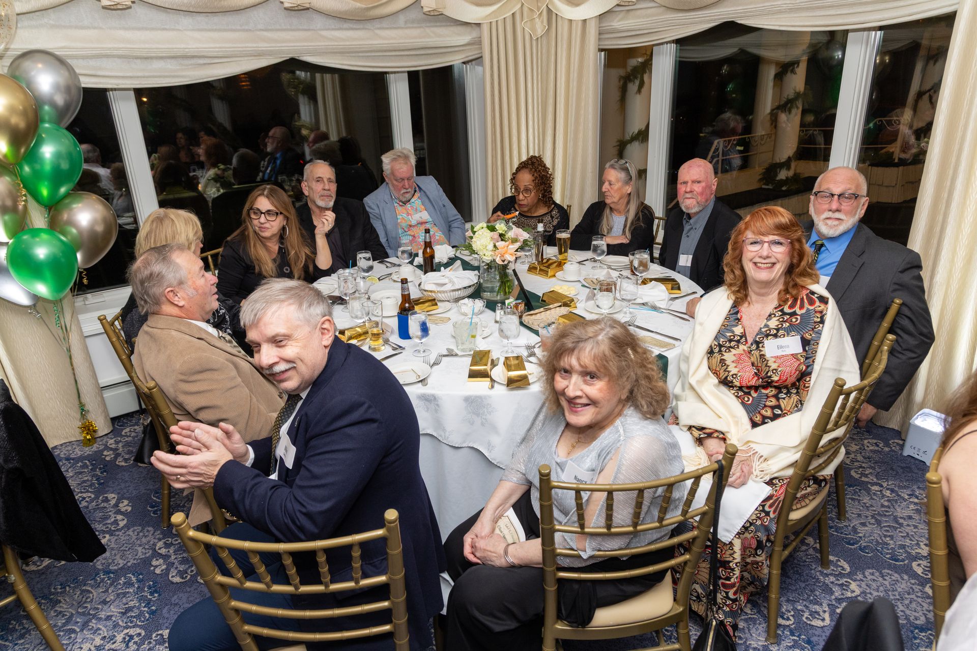 A group of people seated around a table at a formal event, balloons in the background.