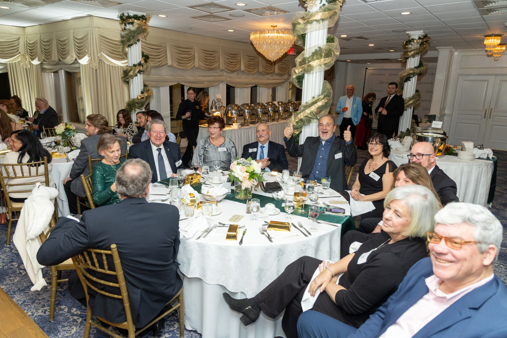 People seated at round tables in a decorated dining room. Some are smiling, and one man gestures.