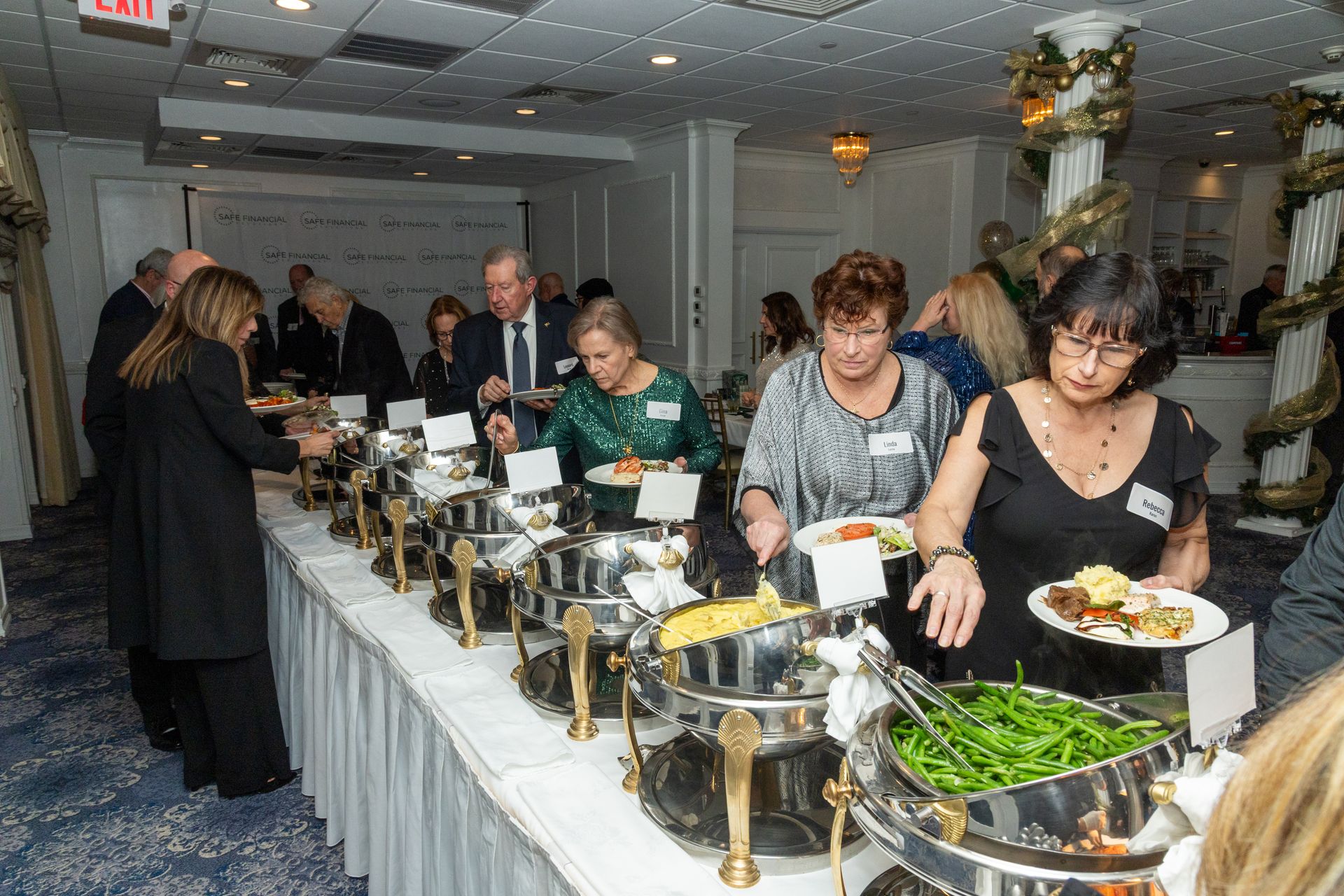 People at a buffet, serving themselves food. Setting is an event hall with decor.