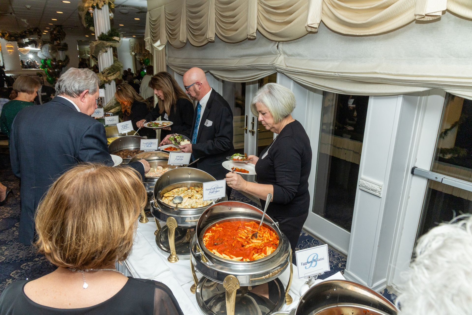 People at a buffet, selecting food from chafing dishes at an event.