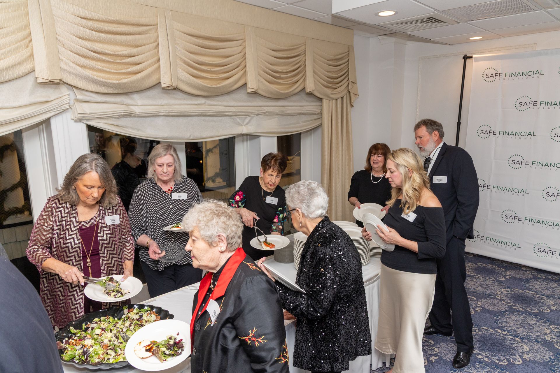 People at a catered event; buffet table with food; white and gold room.