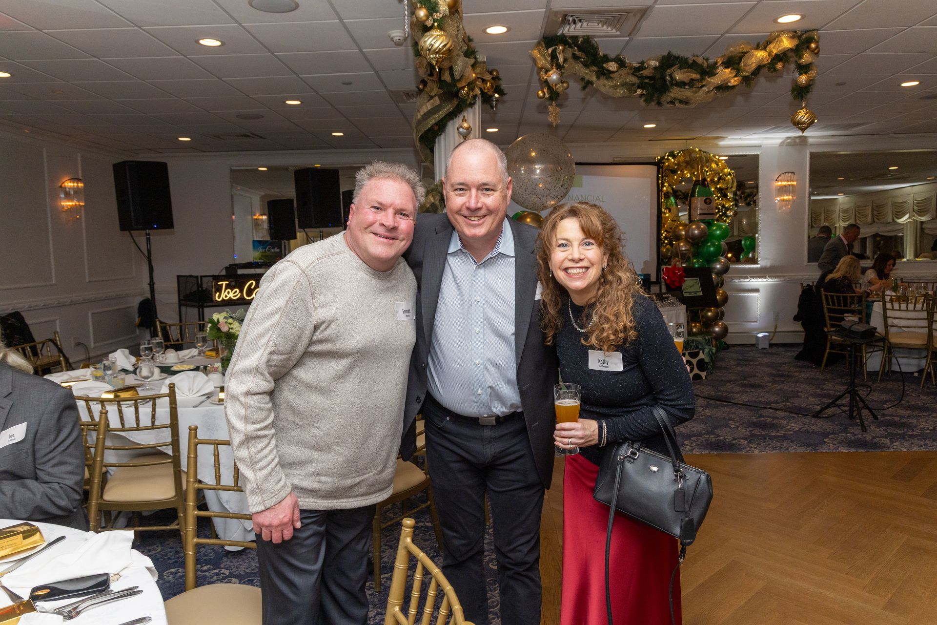 Three people smile, posing together at an indoor event, with decorations and tables.