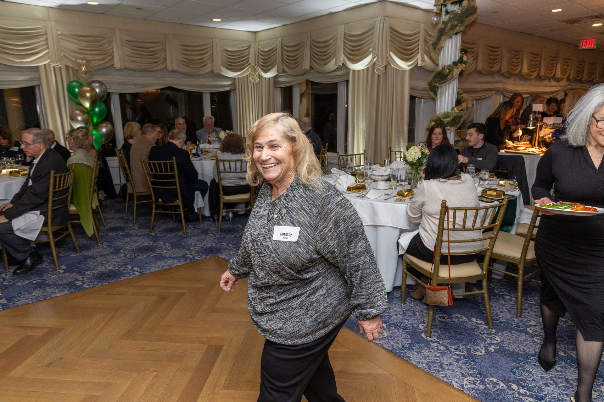 Woman smiles, walks on dance floor in ballroom; guests seated at tables.