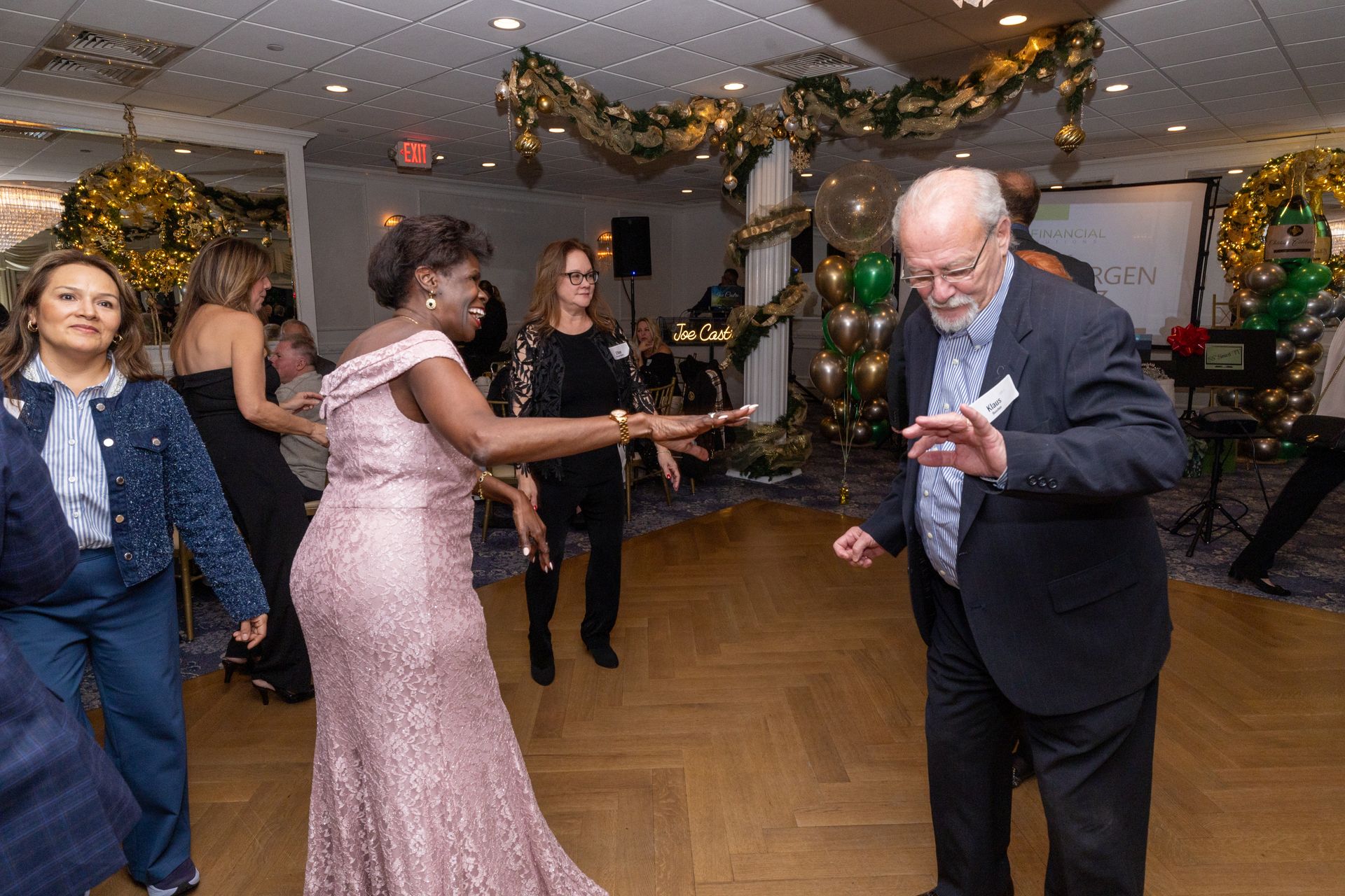 People dancing at a party in a decorated room. A woman in a pink gown dances with a man in a suit.