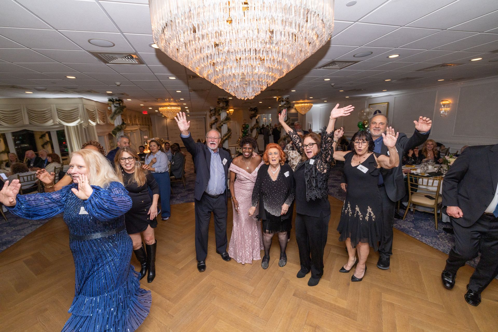 People dancing and celebrating in a ballroom with a chandelier.