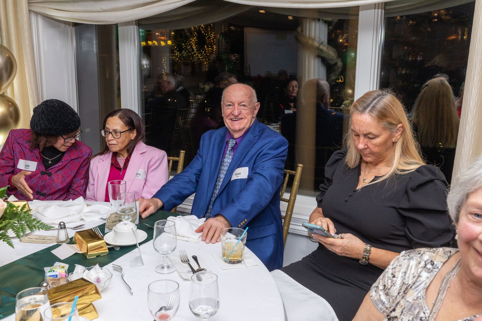 People seated at a table at a formal event, with one person in a blue suit, holding a table napkin.