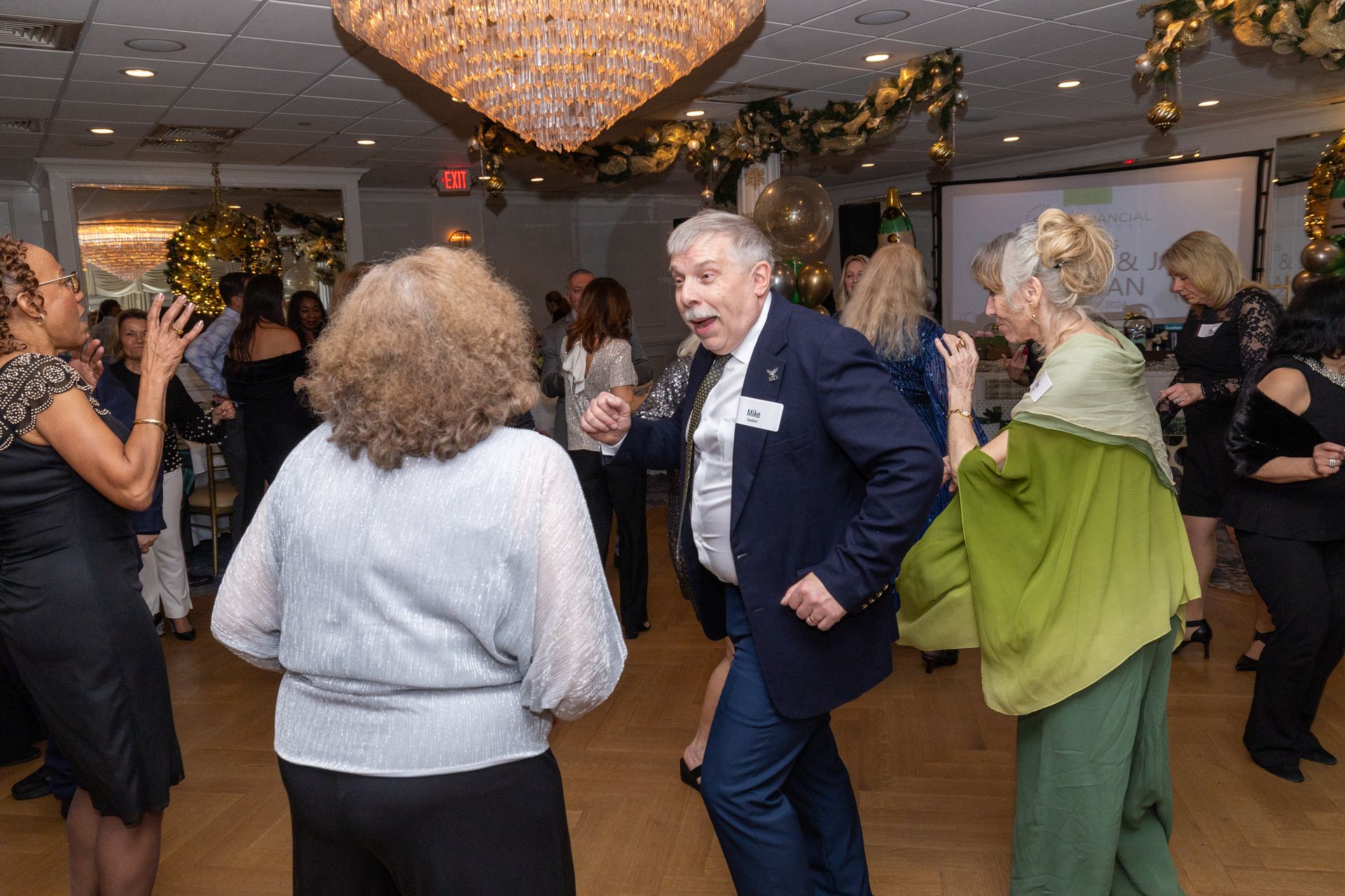 People dancing at a party in a decorated ballroom. A man in a blue blazer dances enthusiastically.