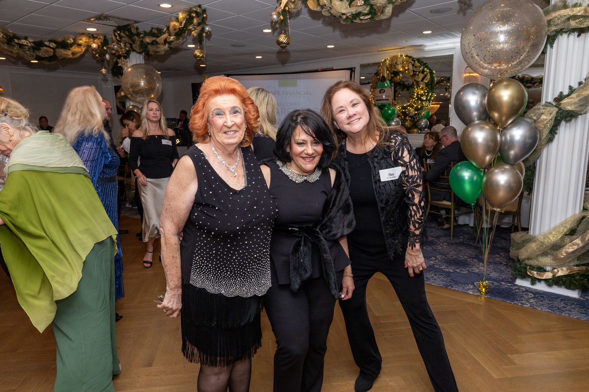 Three women pose at an event; festive decorations with balloons.