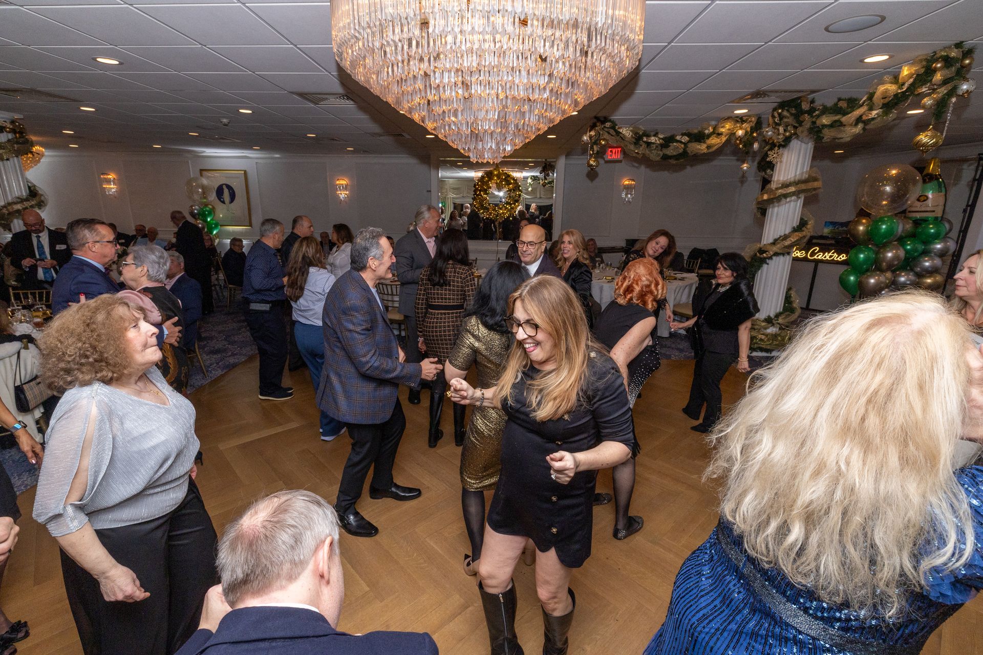 People dancing in a decorated ballroom with a chandelier and balloons.