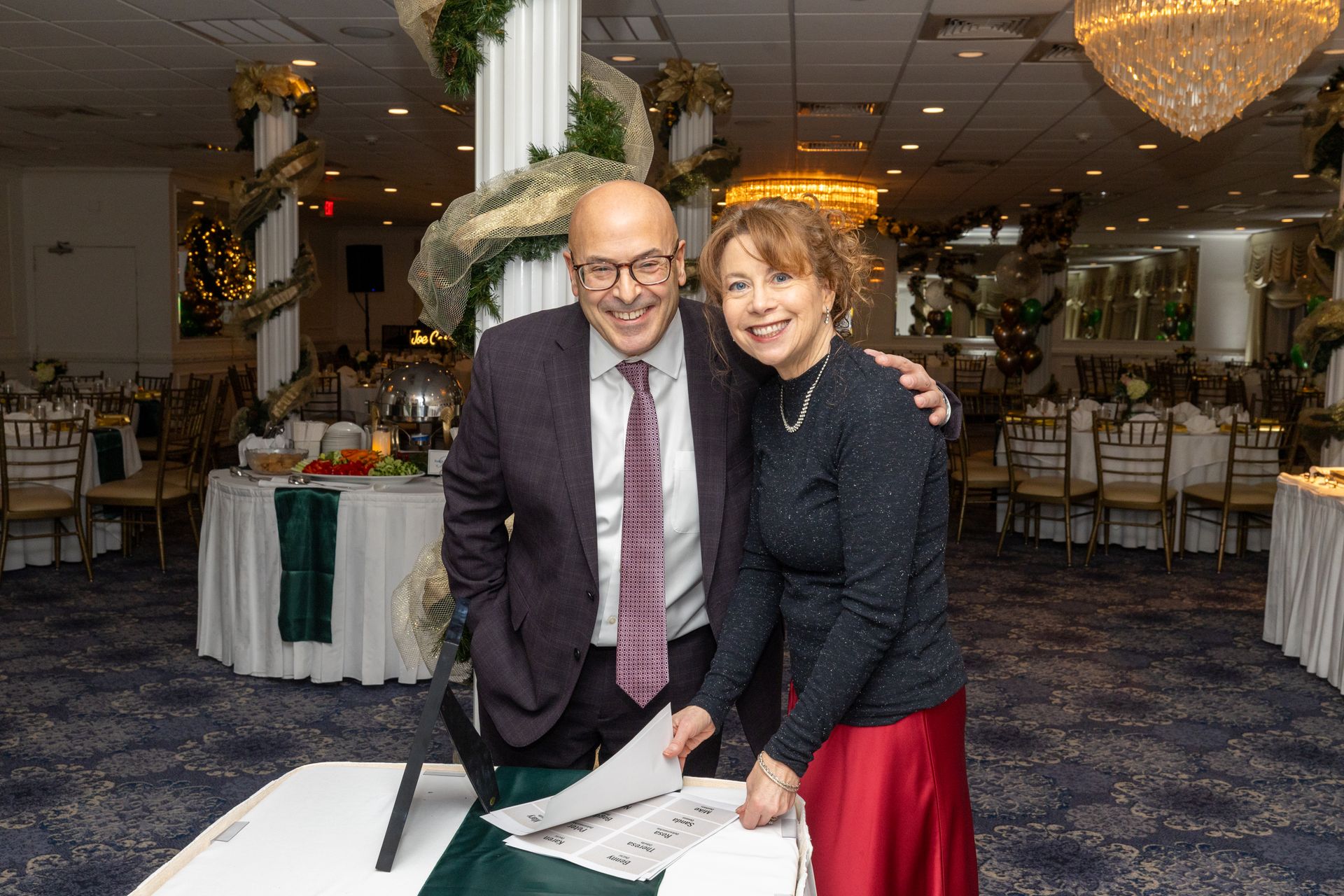 Couple smiles, looks at documents on a table in a decorated ballroom.