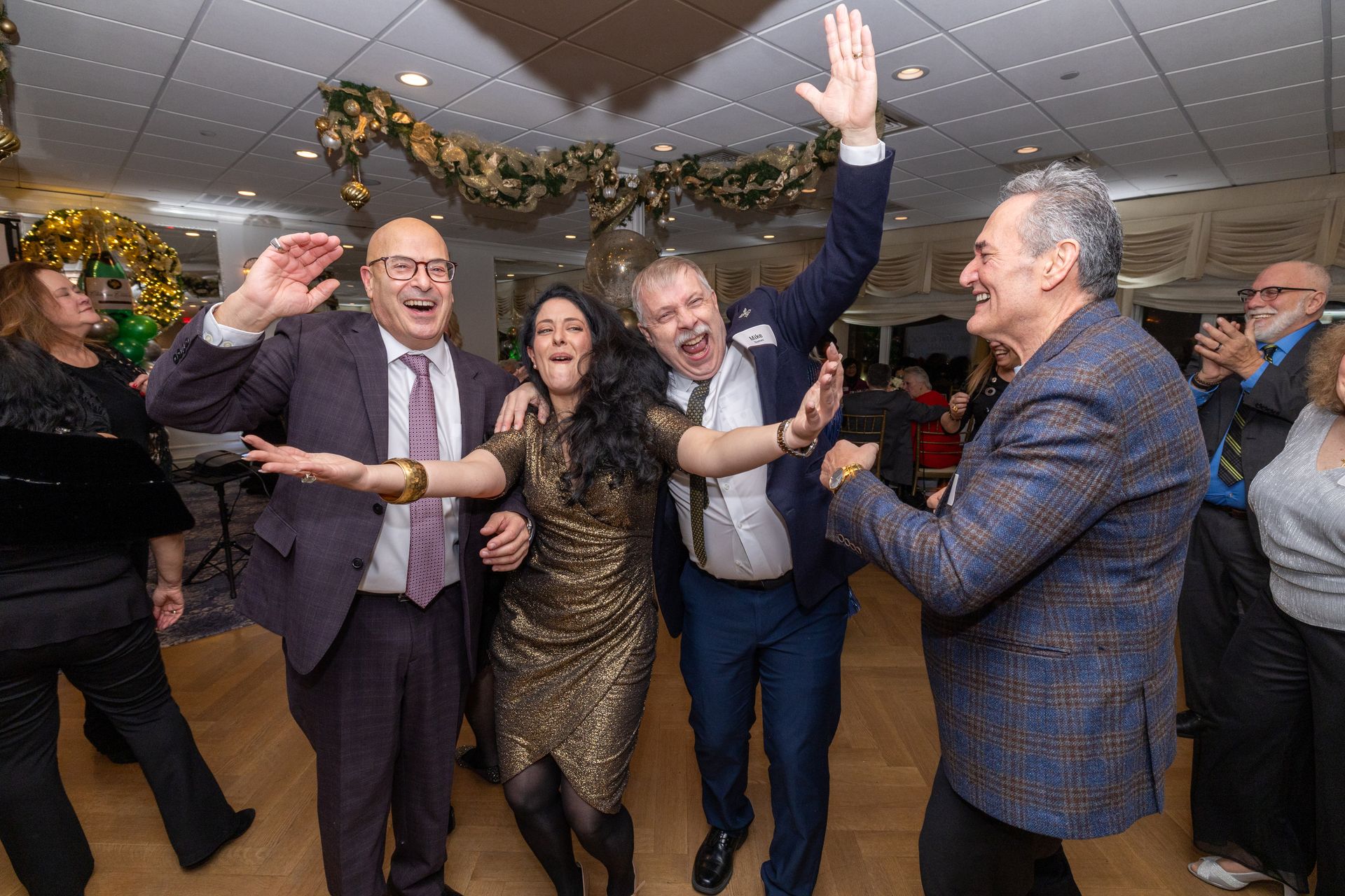 People dancing enthusiastically at a party, raising arms. Glittering decorations, warm lighting.