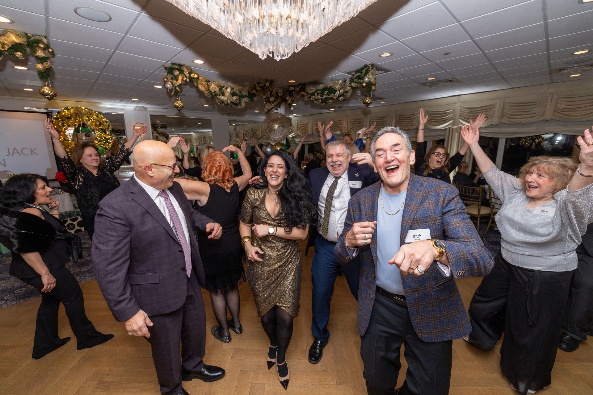 People dancing and celebrating at a party with gold and white decorations.