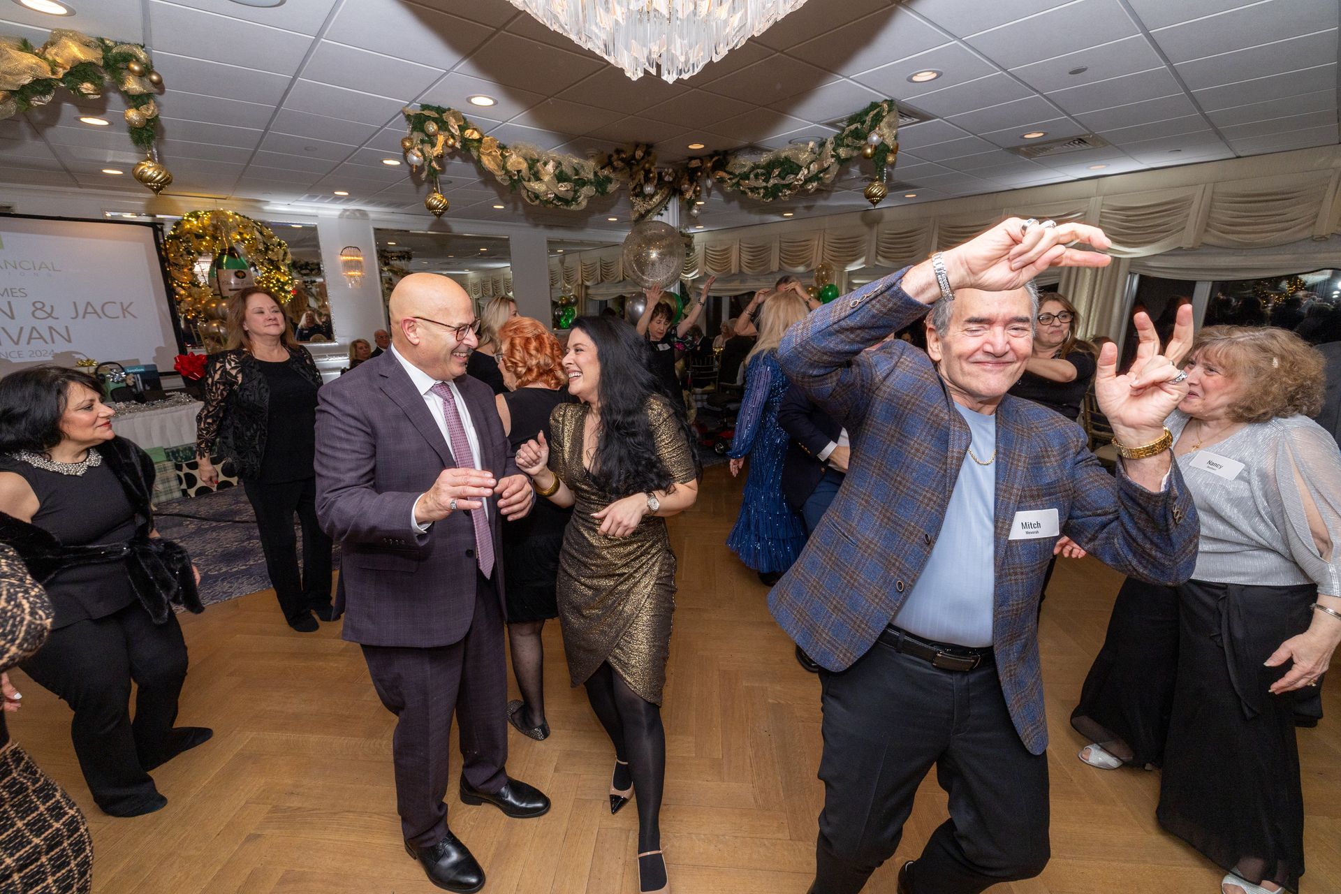 People dancing at an event, some with arms raised. Interior with decorations, including gold and green.
