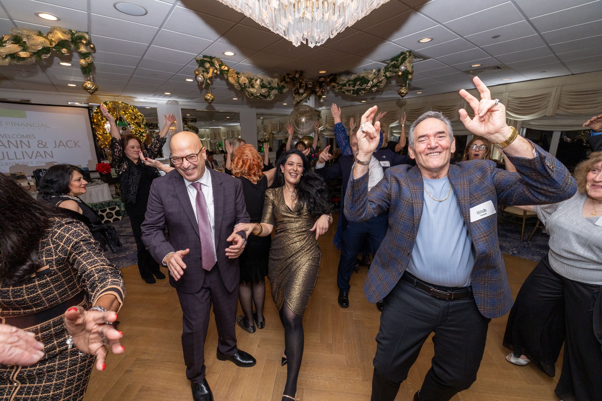 People dancing at an event, arms raised, smiles, a decorated room with gold accents.