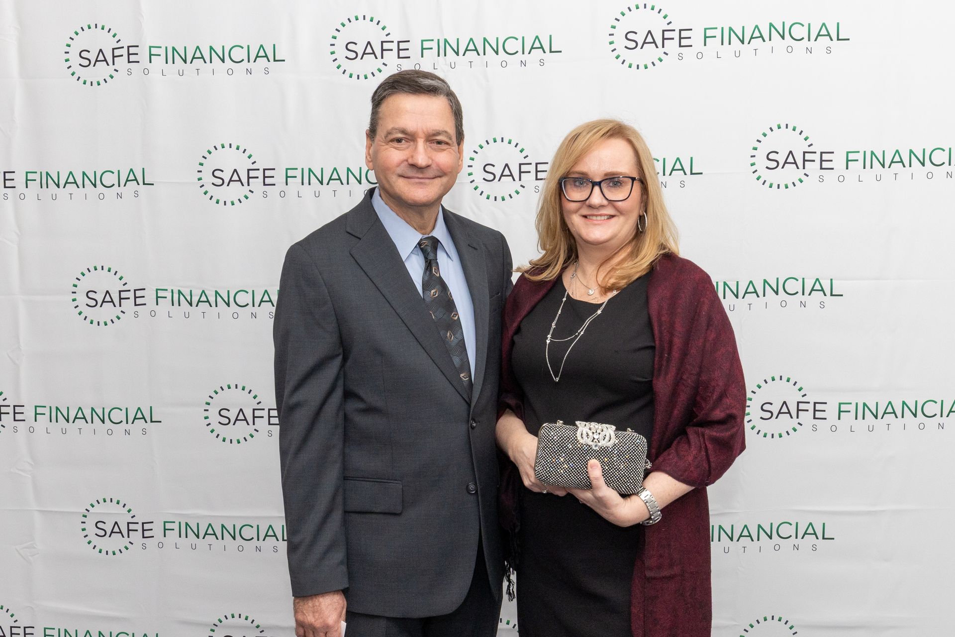 A man and woman pose in front of a backdrop with a 