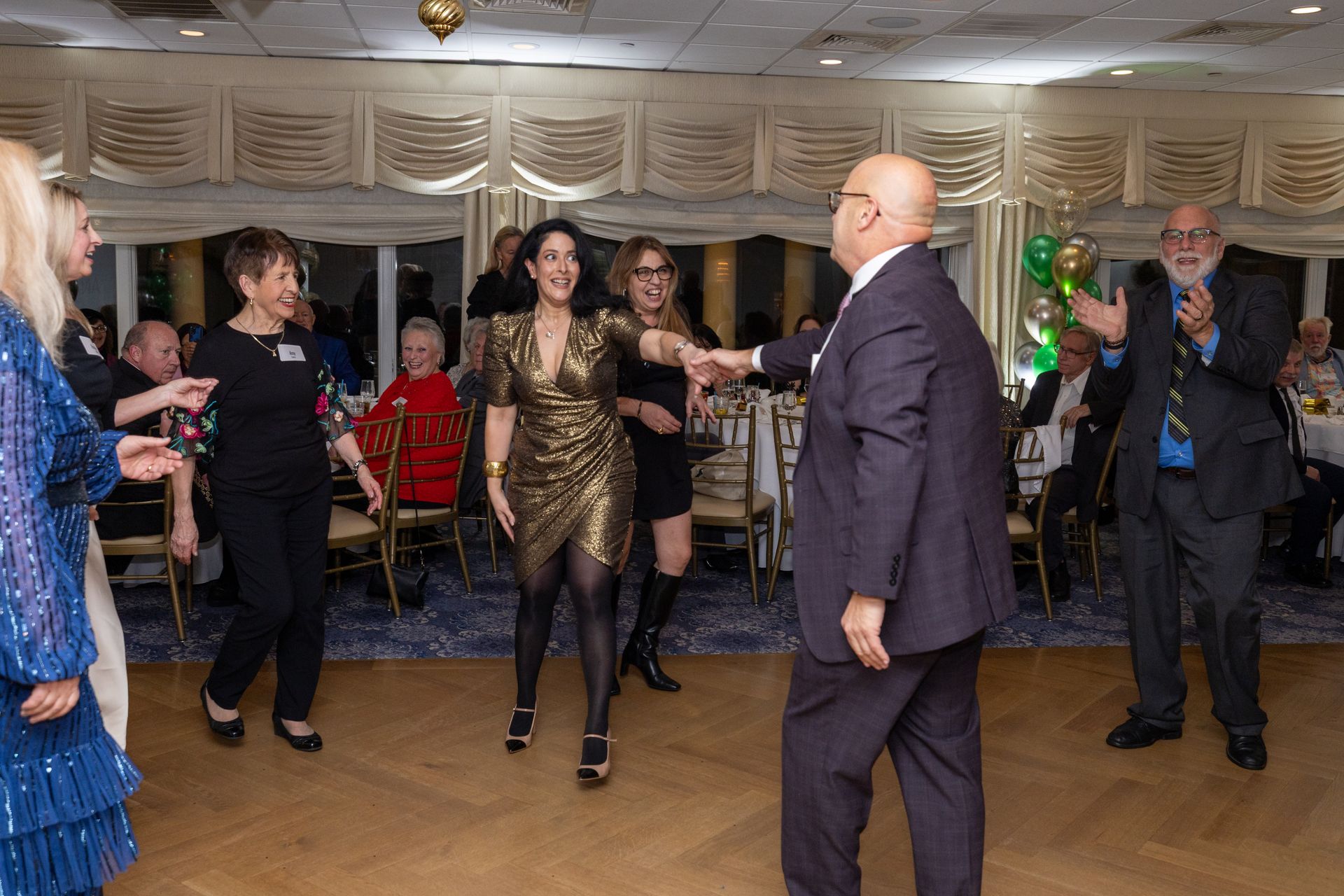 People dancing at a party in a decorated room with gold and green accents.