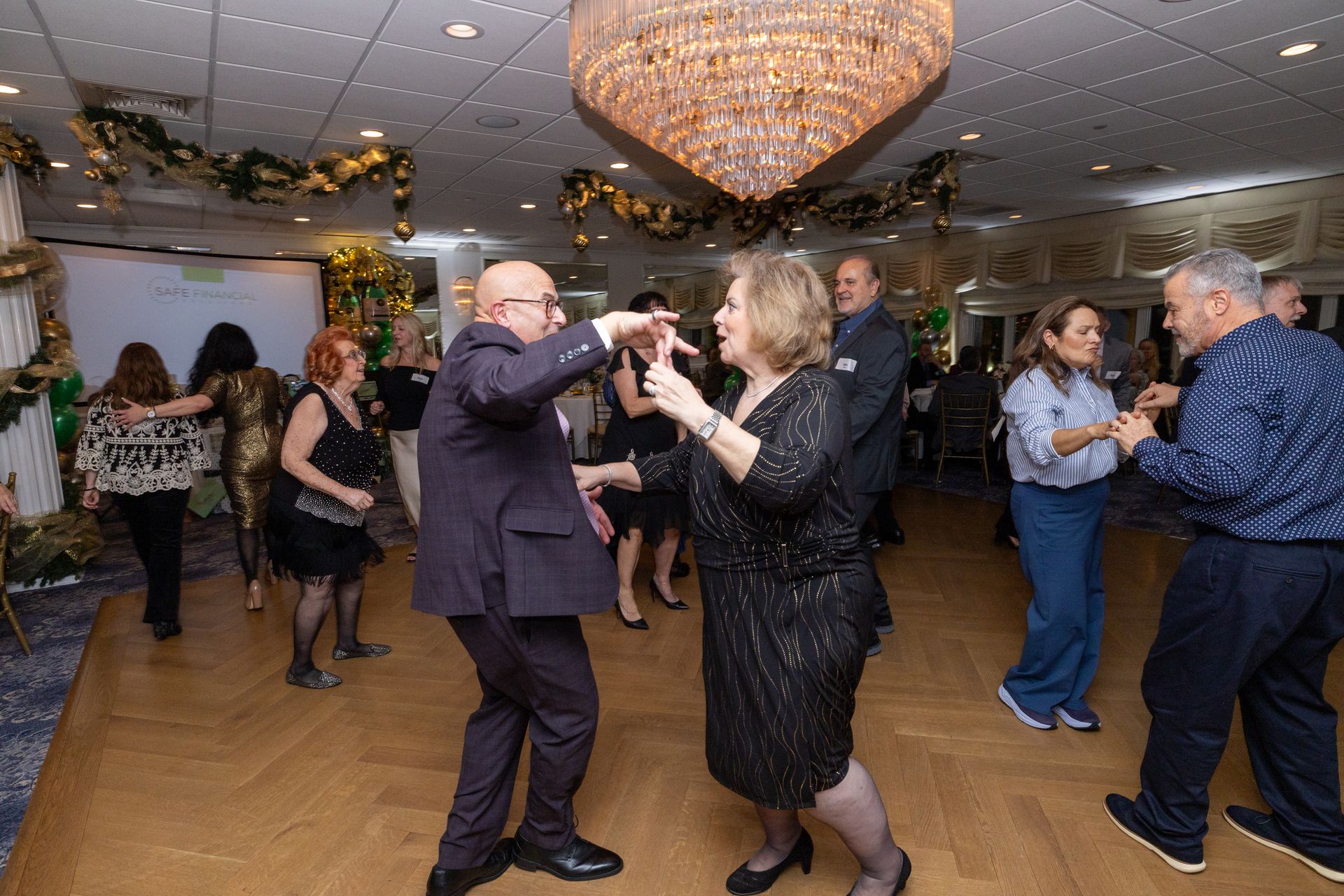 People dancing at a party under a large chandelier. Festive decorations adorn the ceiling and walls.