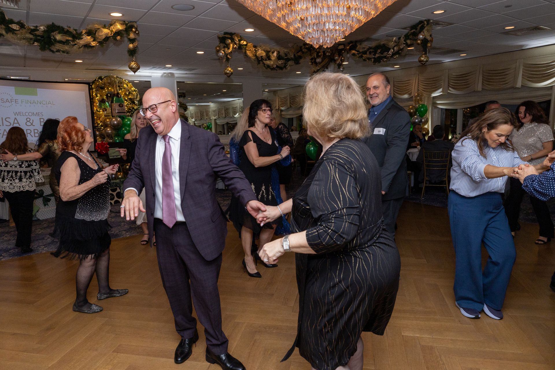 People dancing in a decorated ballroom. A man in a suit dances with a woman in a sparkly dress.