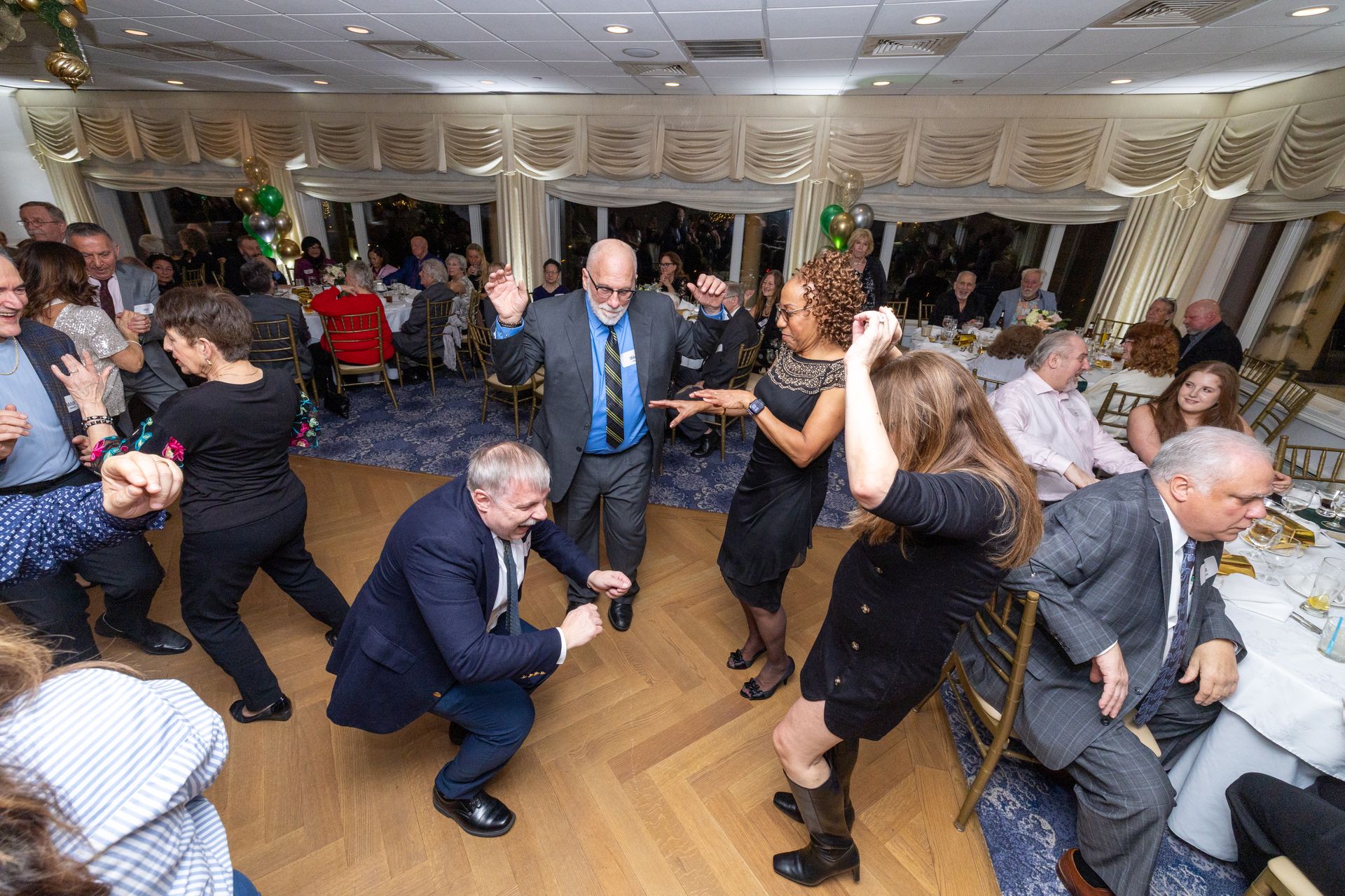 People dancing at a party in a room with windows and decorations.
