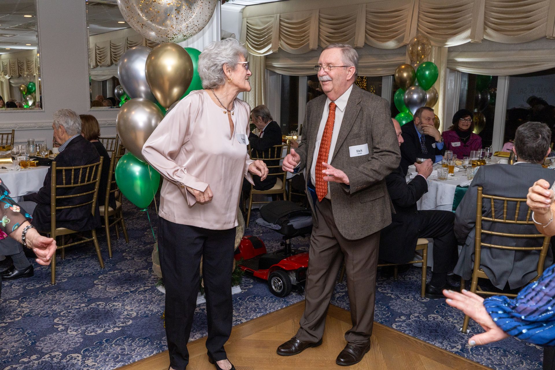 Couple dancing at a party; balloons, tables, other guests in background.