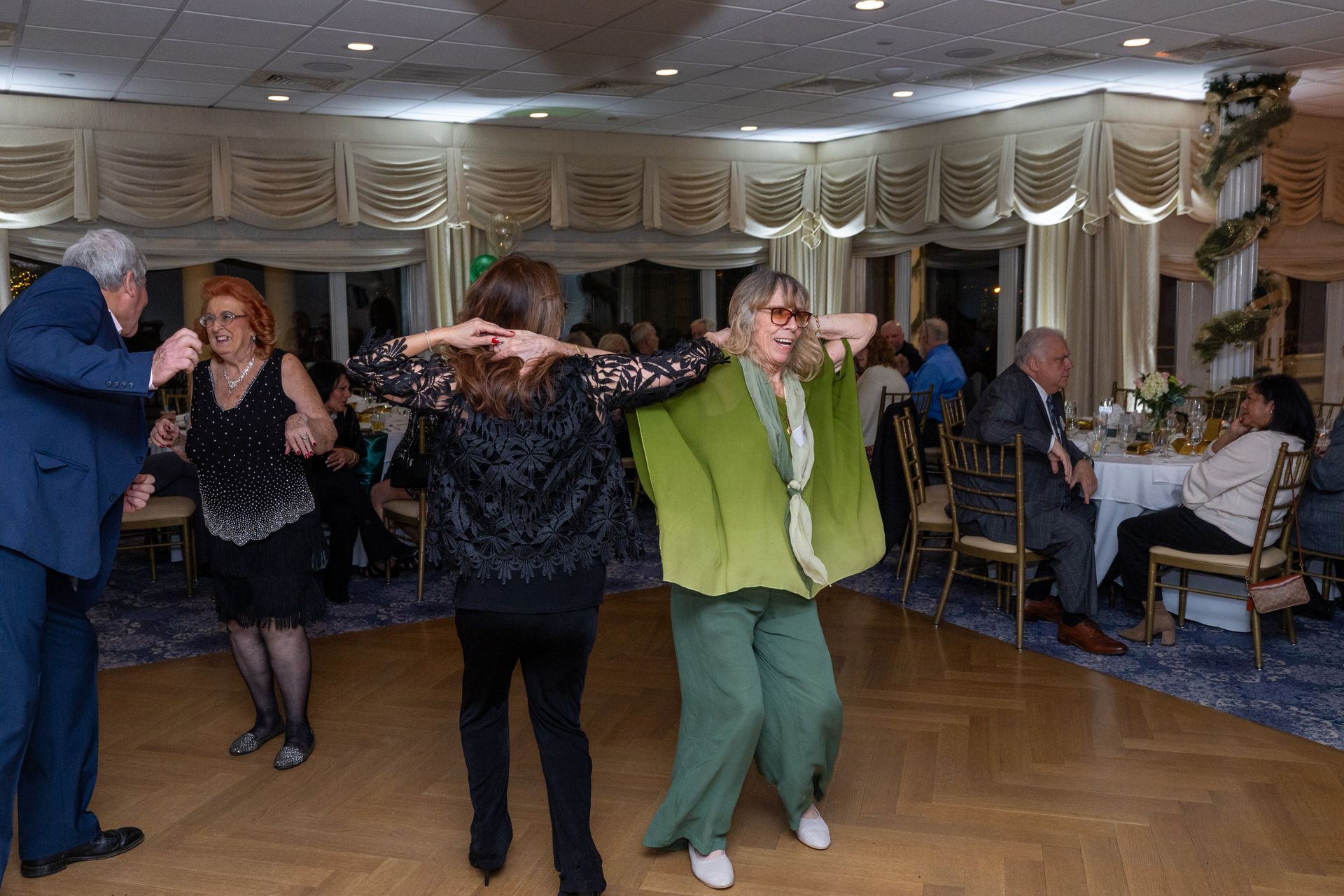 People dancing at a party in a decorated room with tables and chairs.