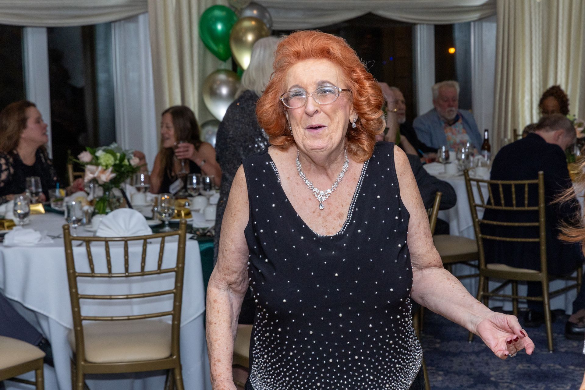 Woman with red hair, wearing a black sparkly top, at a party, smiling.