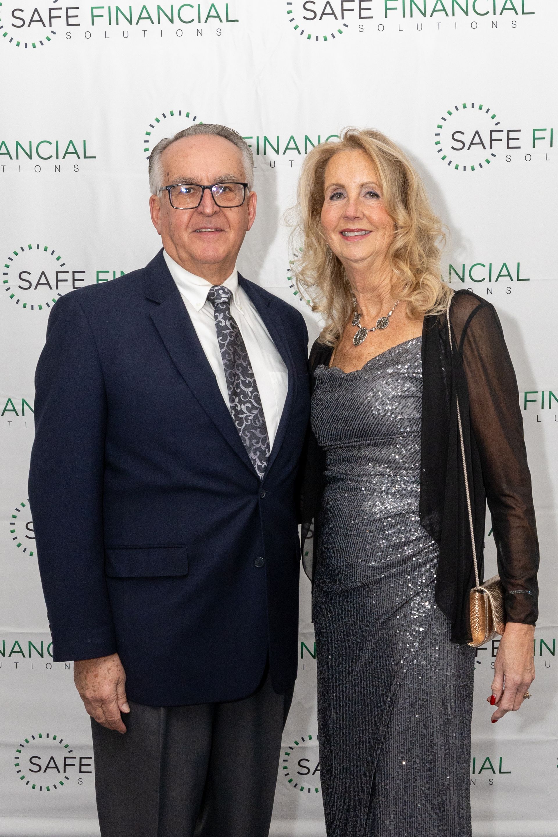 Man and woman posing at an event with a Safe Financial backdrop. The woman wears a formal gown and the man wears a suit.