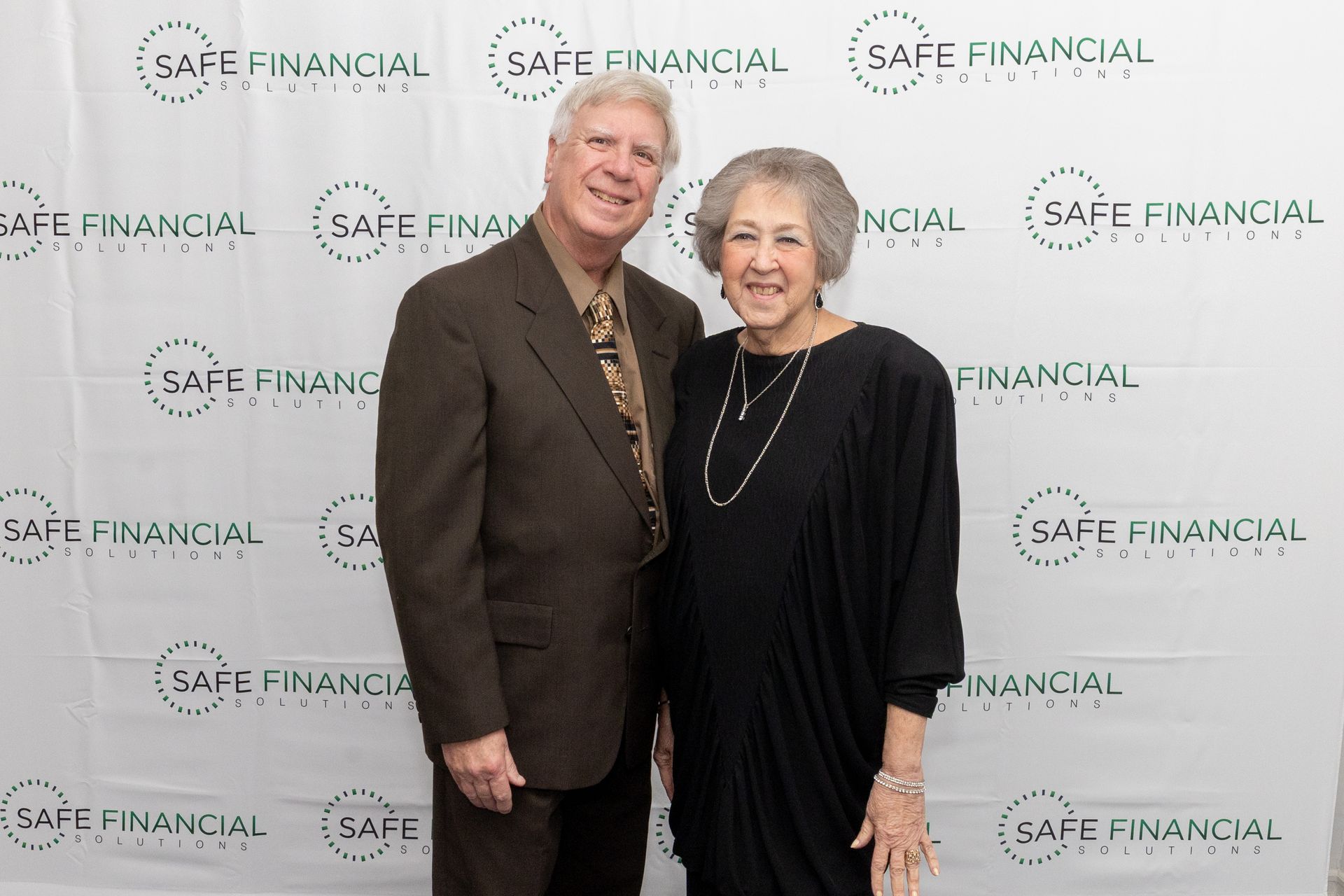 A man and a woman pose in front of a backdrop with the words 