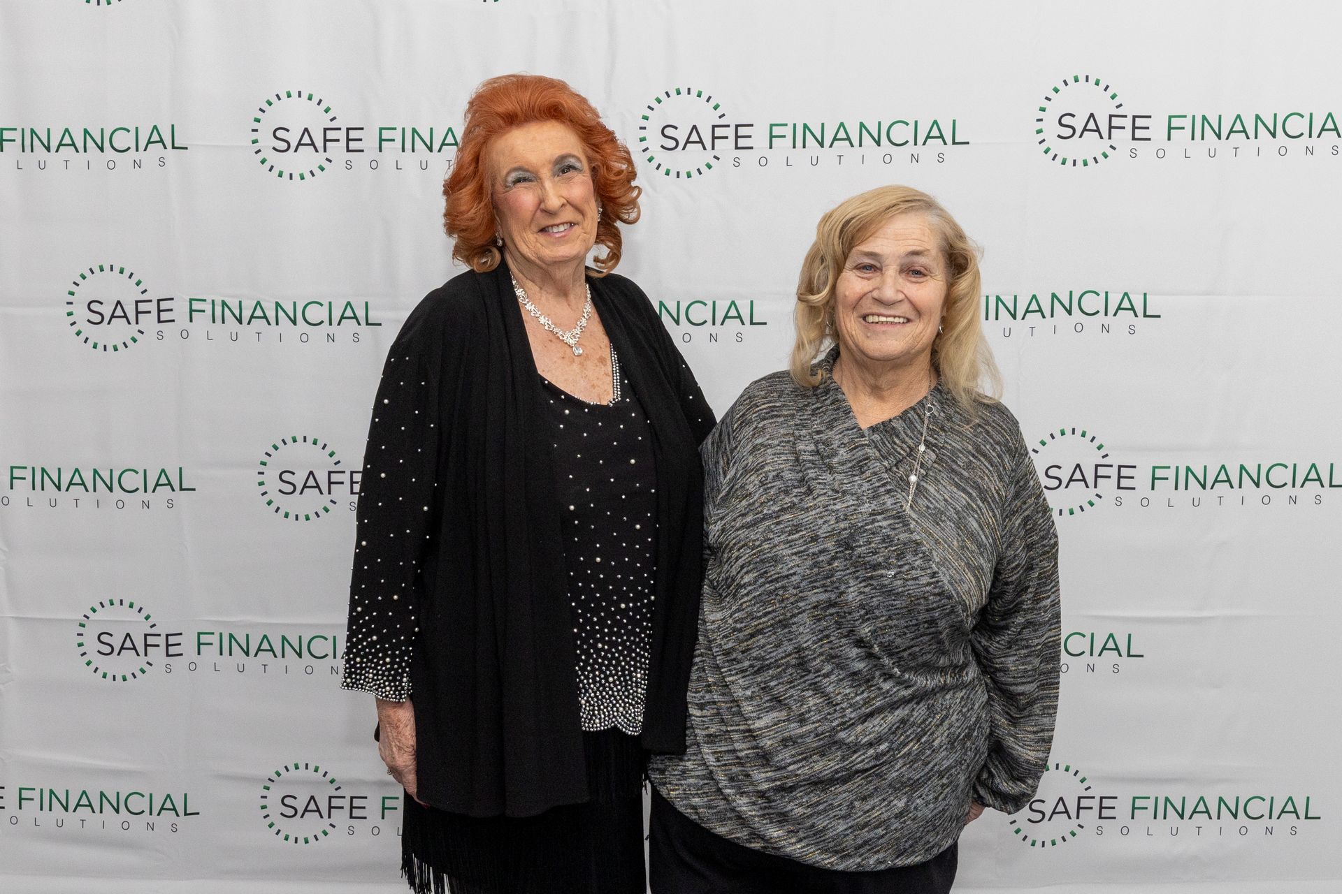 Two women stand in front of a backdrop that reads 