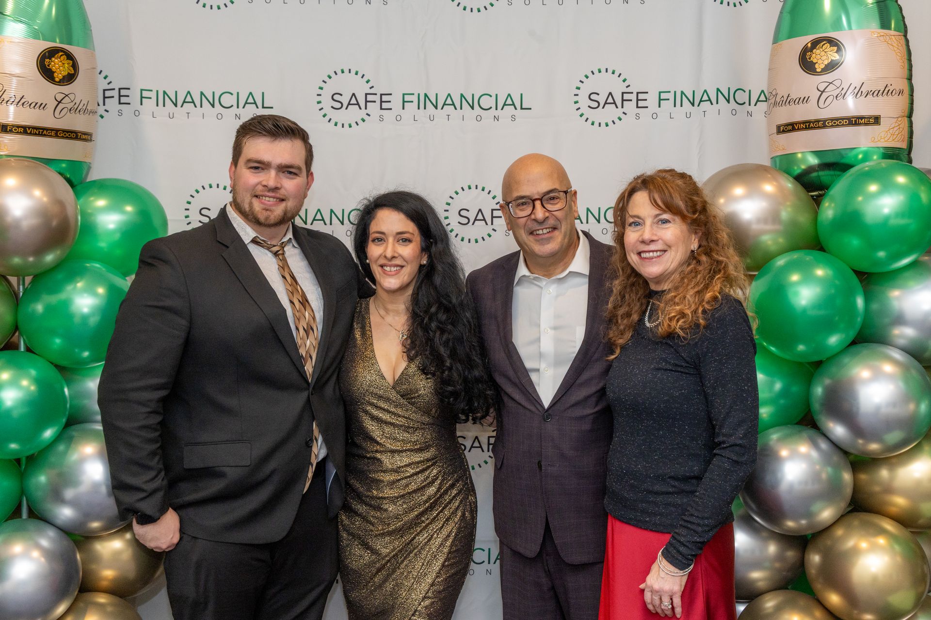Four people posing for photo at event, in front of a backdrop with balloons.