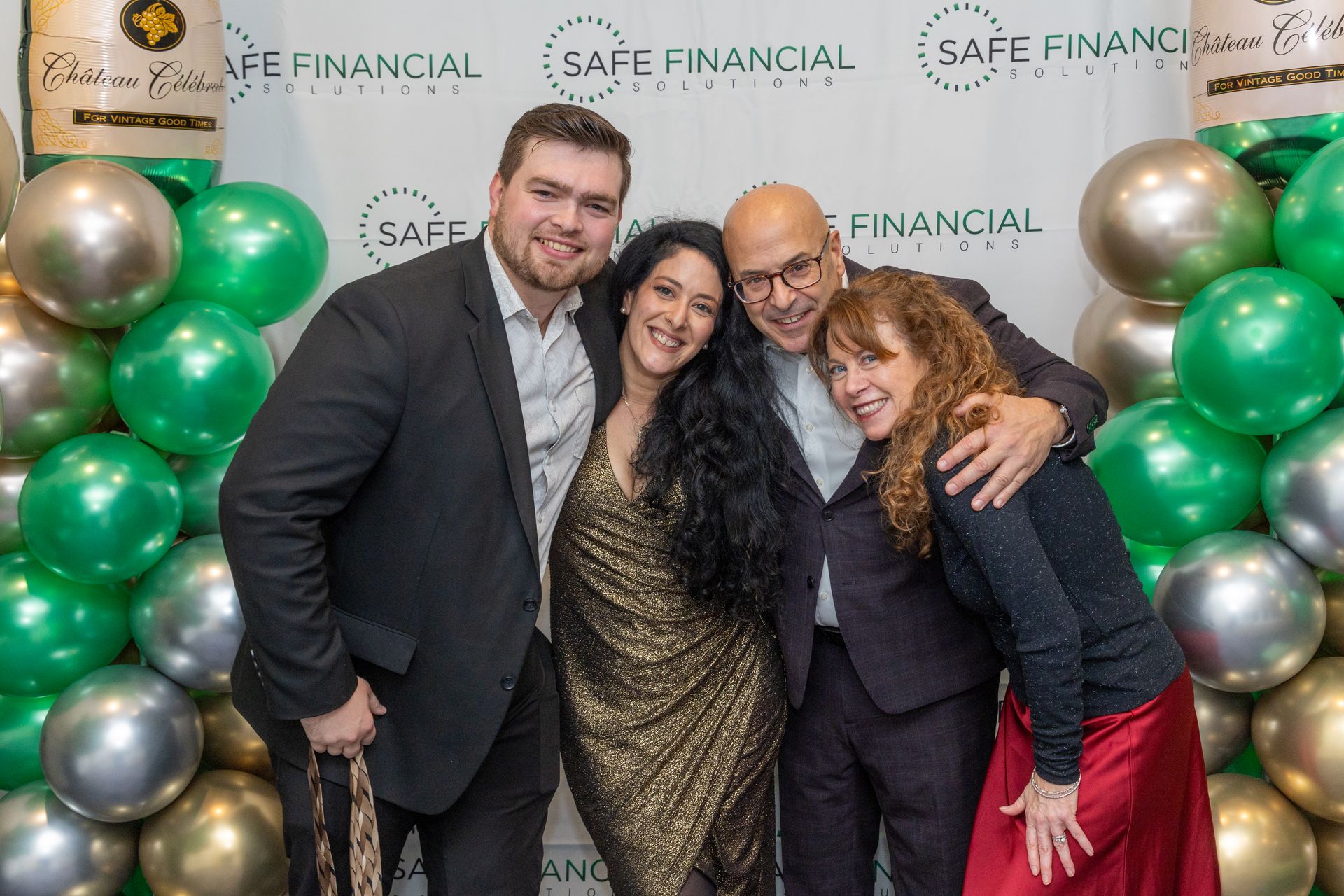 Four people smiling, posing in front of balloons and a 