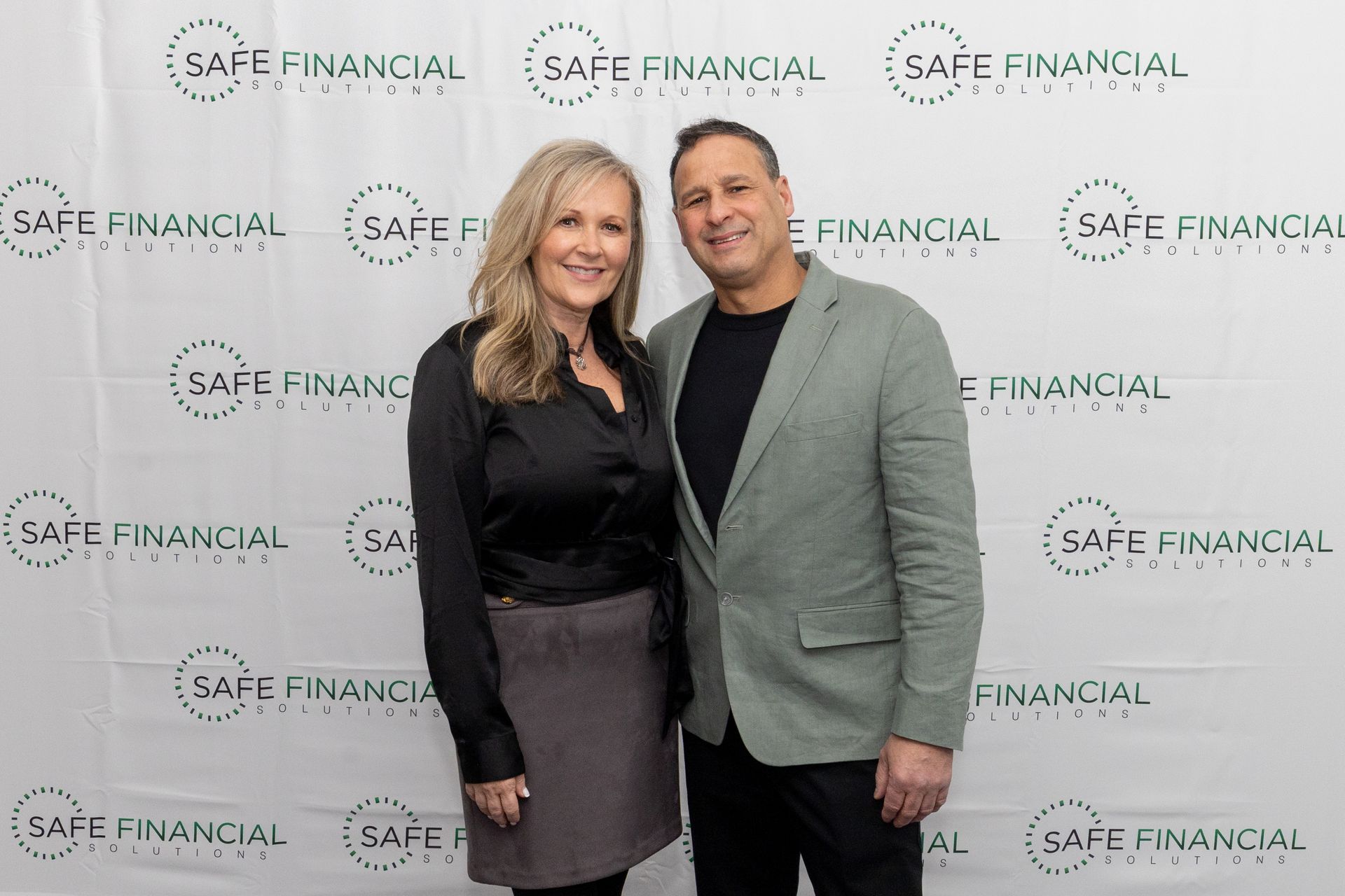 A woman and a man pose in front of a backdrop with a repeating logo 