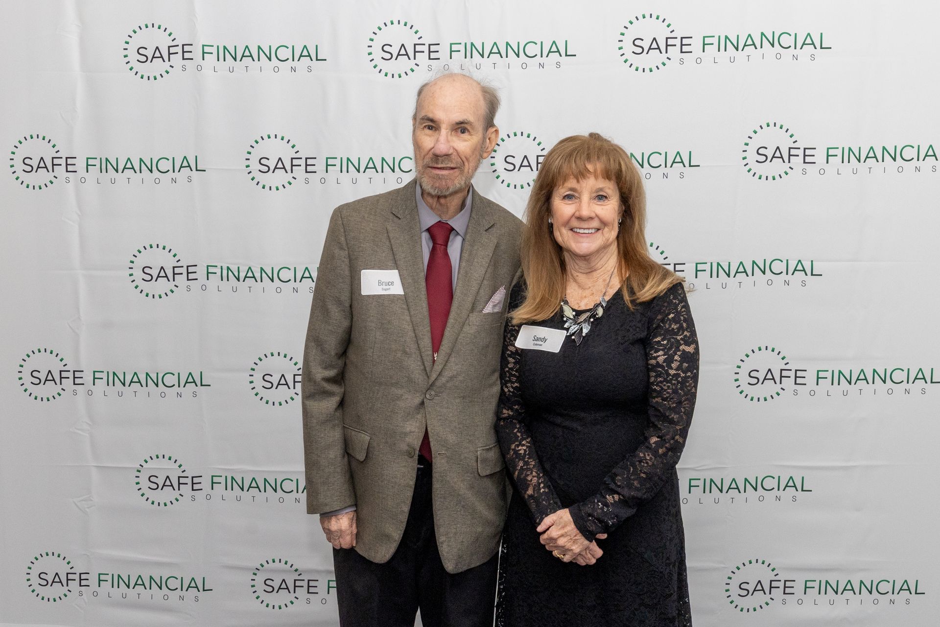 Man and woman pose in front of a backdrop with repeated 