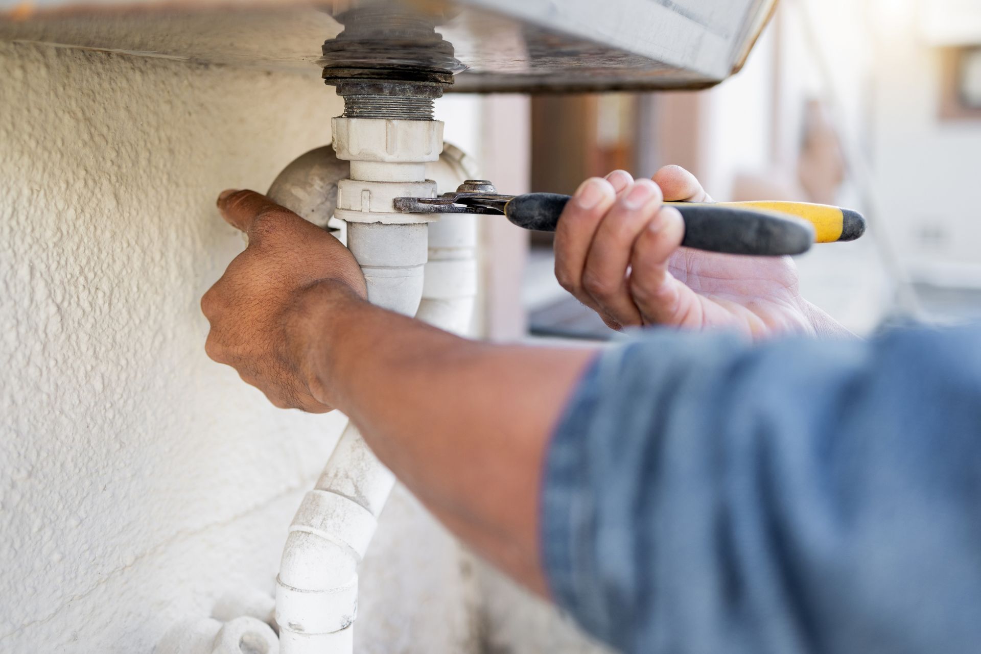 Person tightening a white pipe fitting with a wrench under a sink