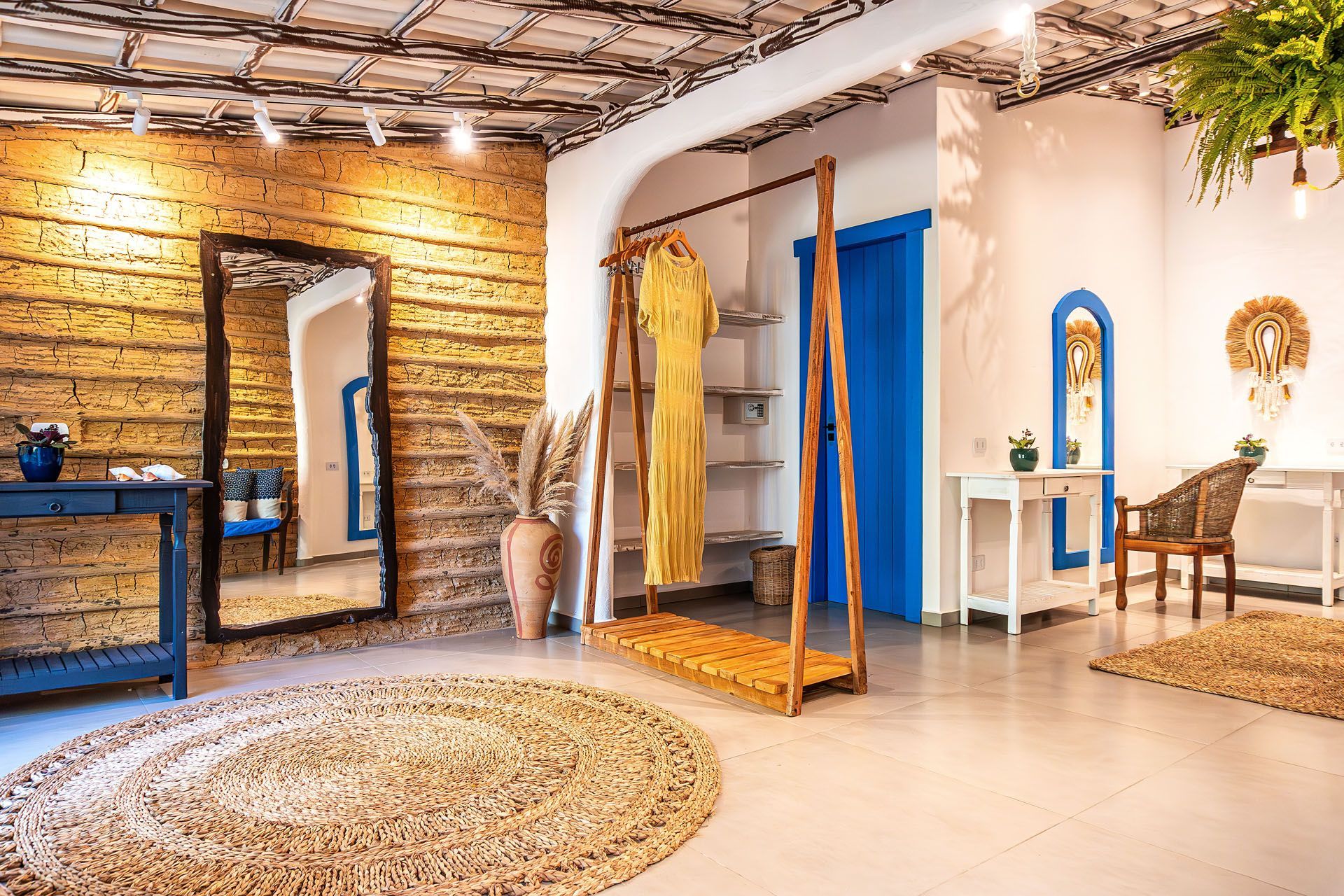 Interior luminoso de boutique com paredes de madeira, espelhos, tapetes, araras de roupas e uma parede de destaque azul.