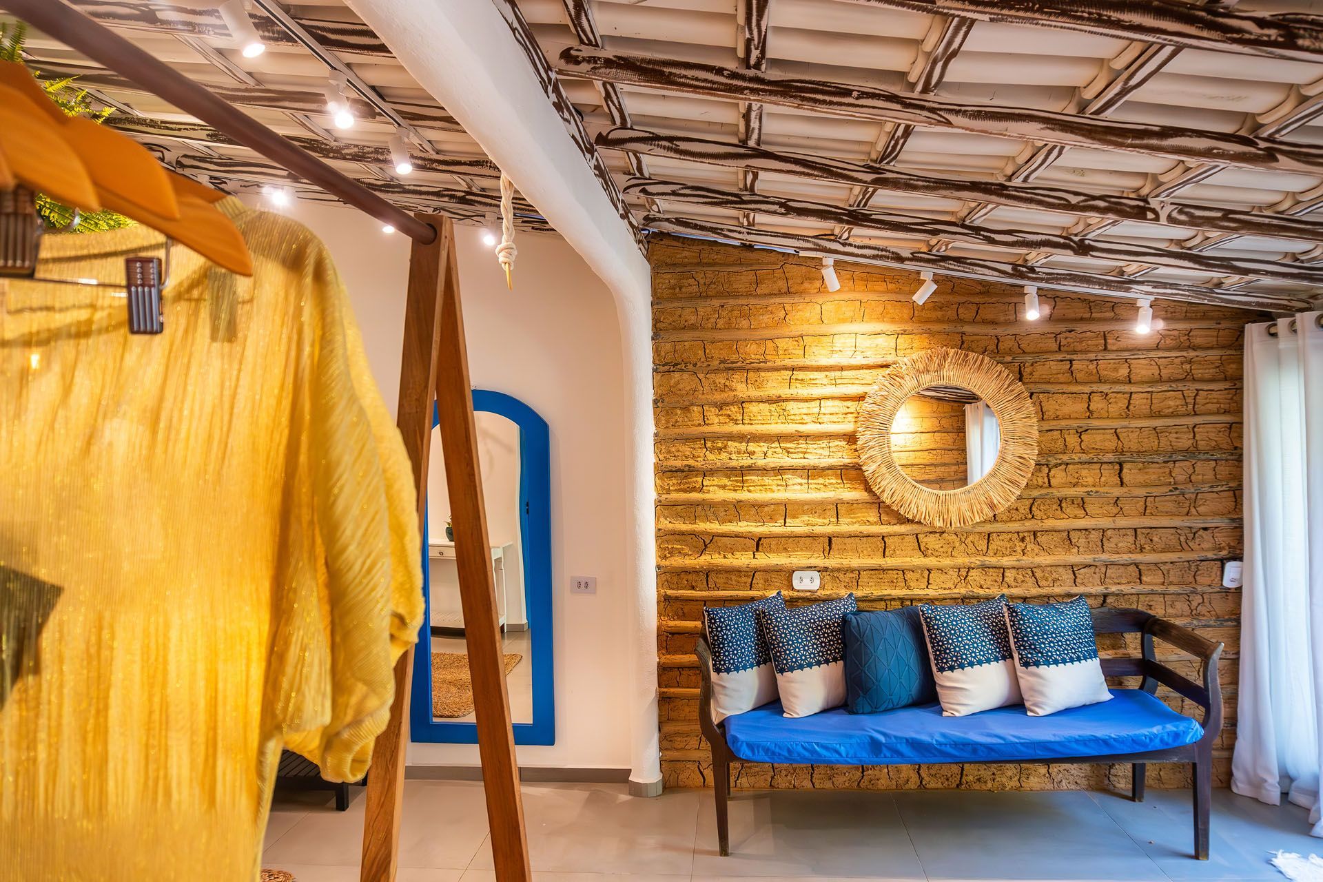 Quarto rústico aconchegante com sofá azul, decoração de parede em vime e tecido amarelo pendurado.