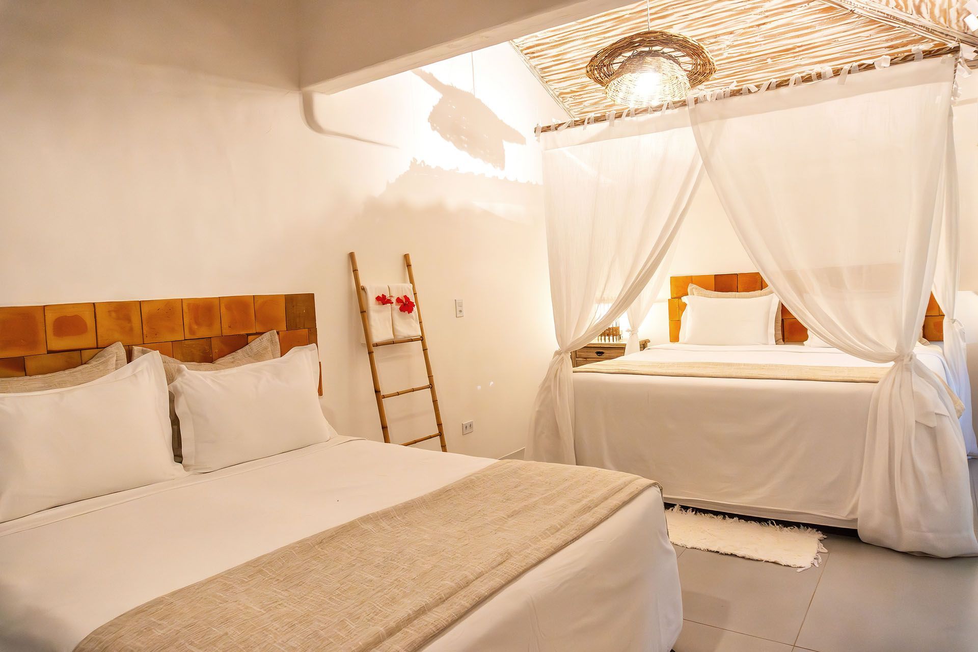 Quarto elegante em tons de branco com duas camas de solteiro, cortinas de dossel transparentes e detalhes ornamentados no teto.