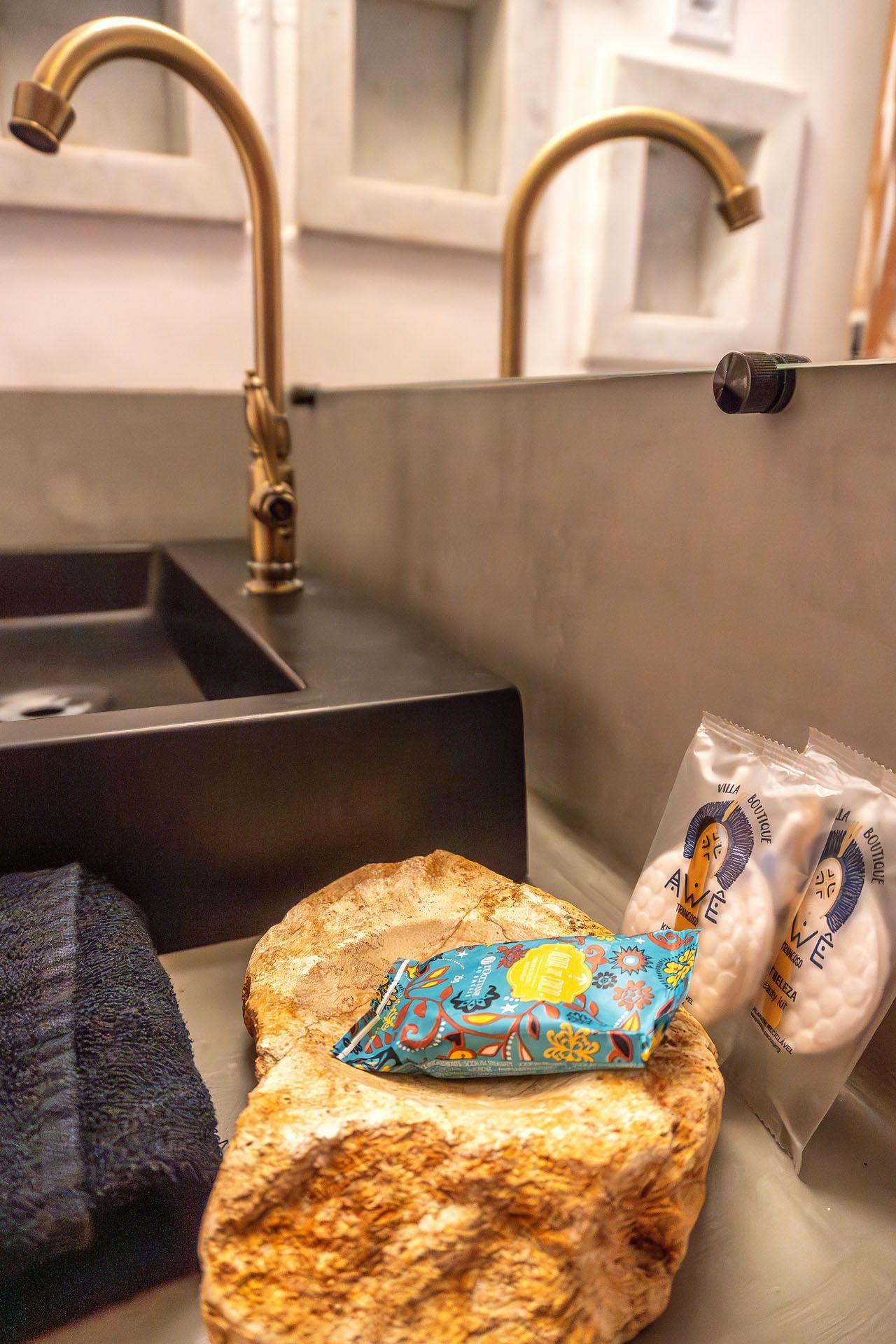 Bancada da cozinha com pão, um pacote de salgadinhos azul, um rolo de papel-toalha e uma torneira dourada ao lado da pia.