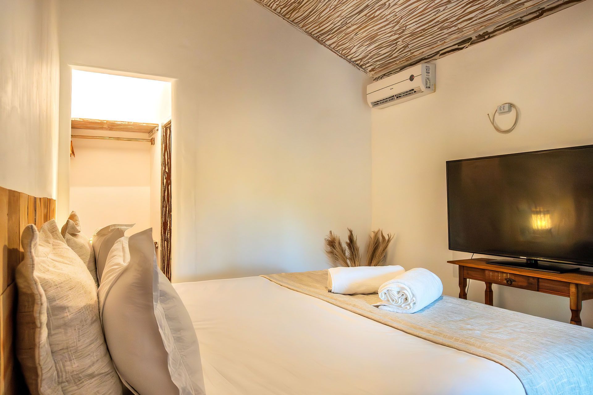 Quarto aconchegante com cama, TV de parede e decoração de teto em tecido trançado em tons neutros e quentes.
