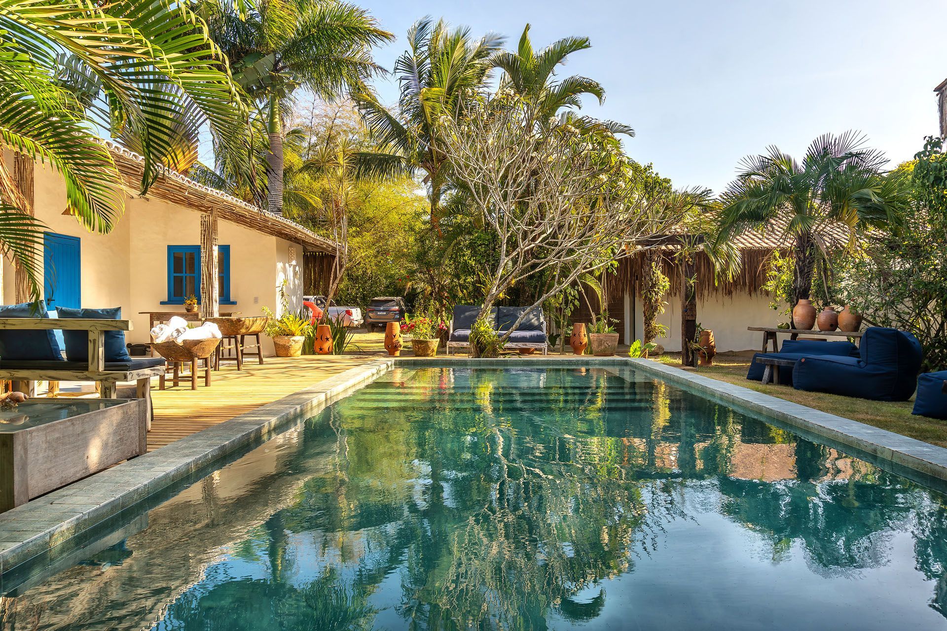Quintal ensolarado com piscina, palmeiras e um pátio com área de estar externa.