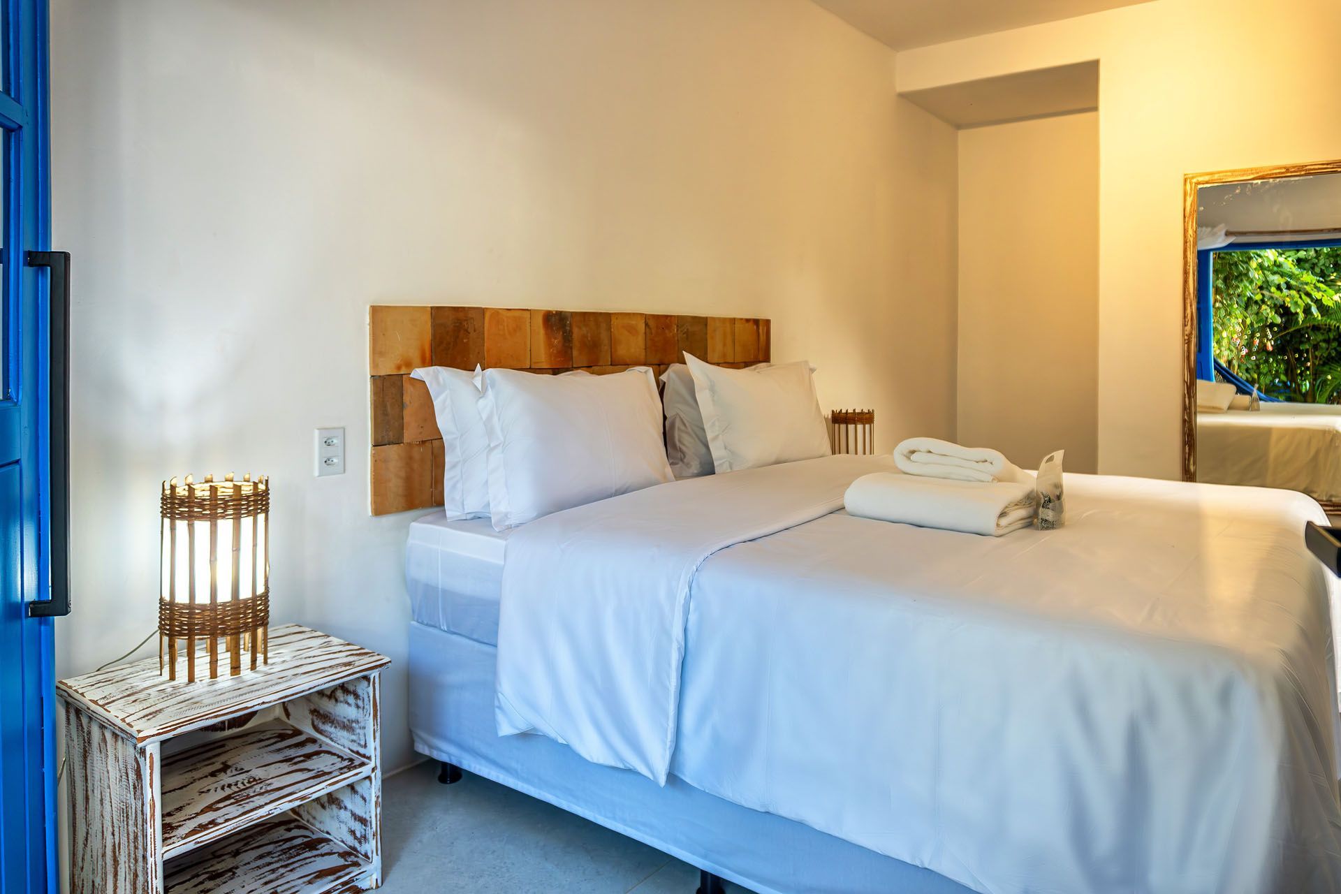 Quarto luminoso com cama branca, luminárias de vime e detalhes em azul perto da janela.