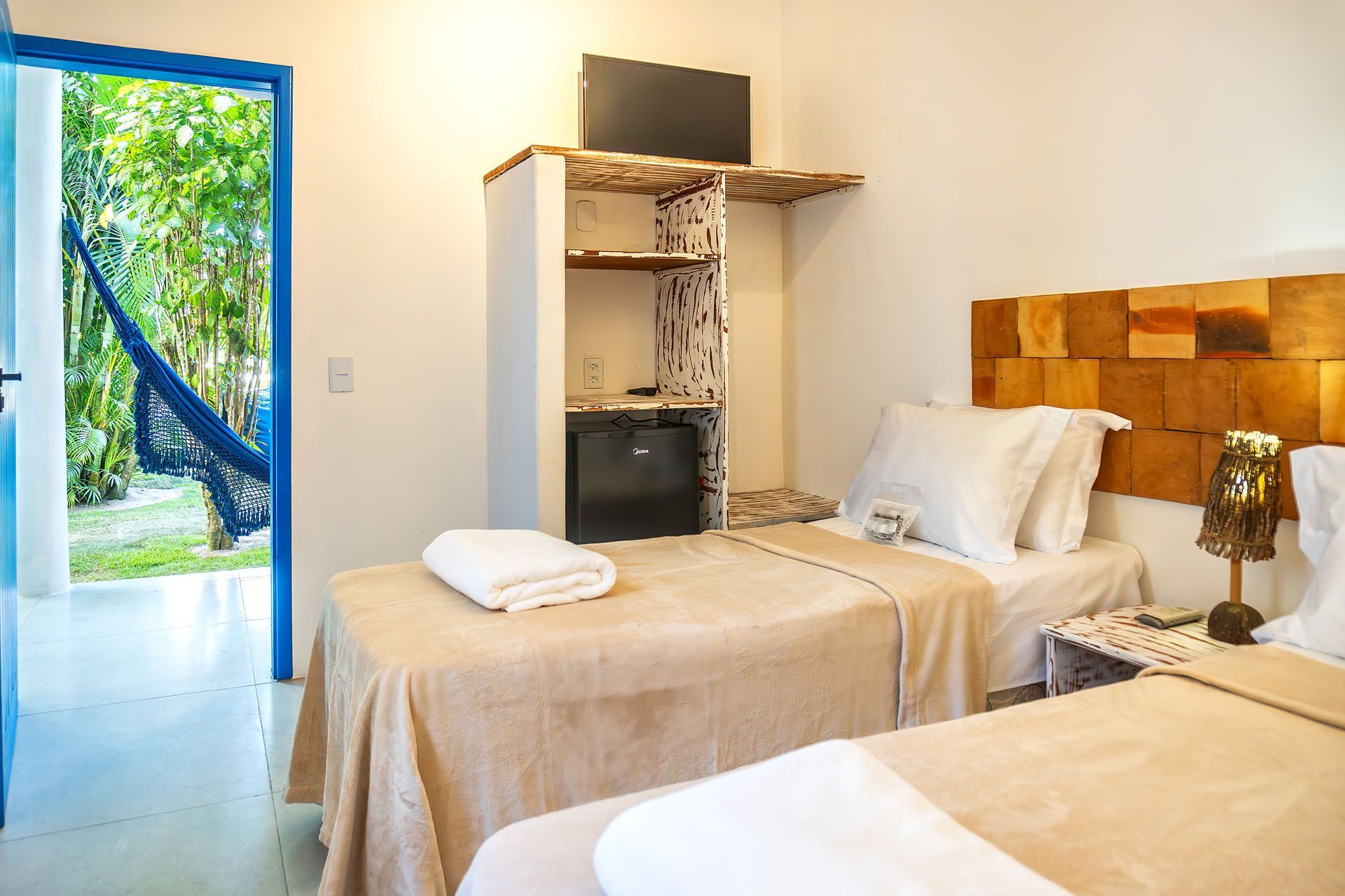 Quarto de casal luminoso com cabeceira de madeira, porta azul aberta e vista para a varanda.