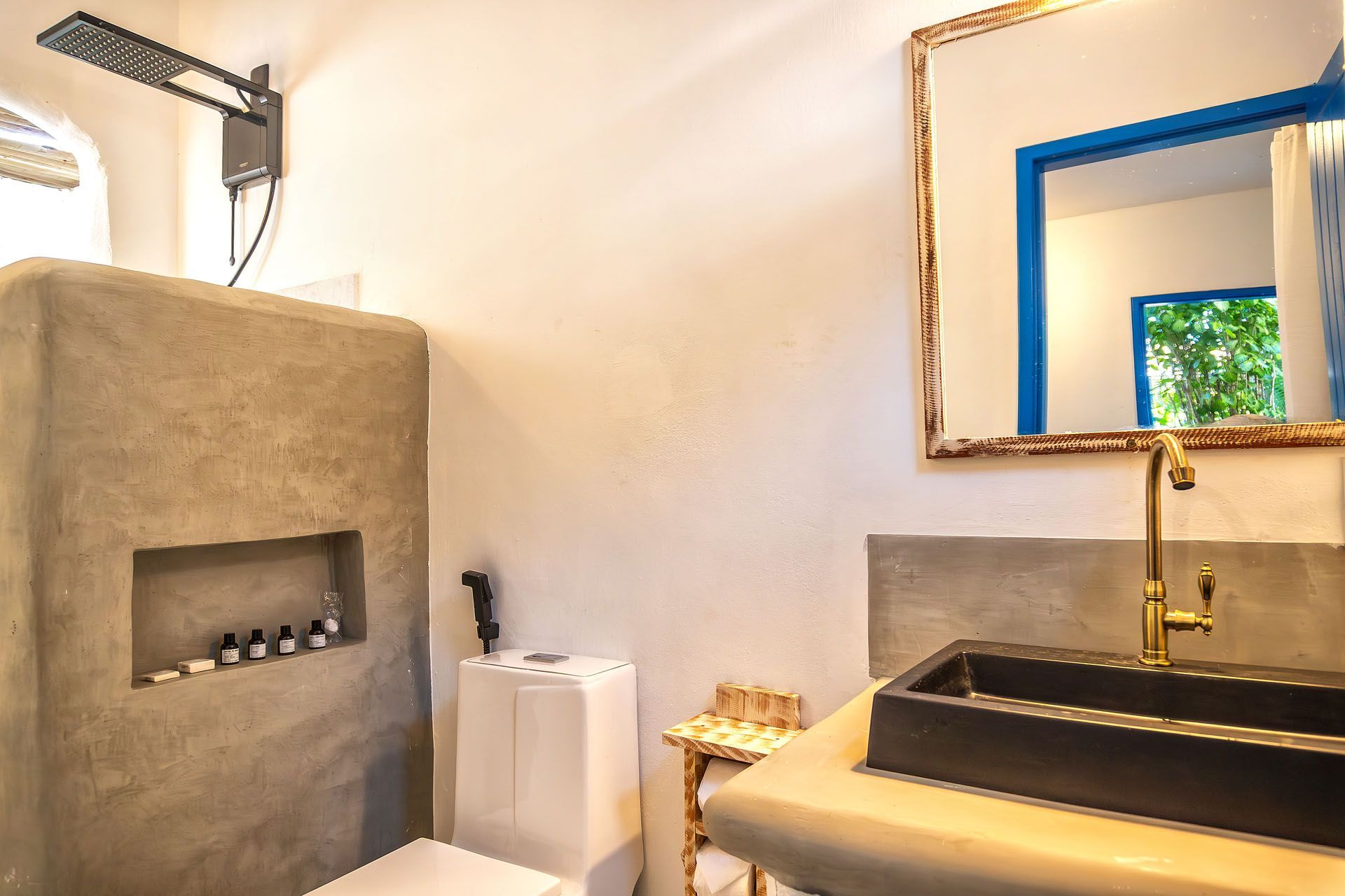 Banheiro moderno com box de concreto, vaso sanitário, pia, metais dourados e espelho com moldura azul.