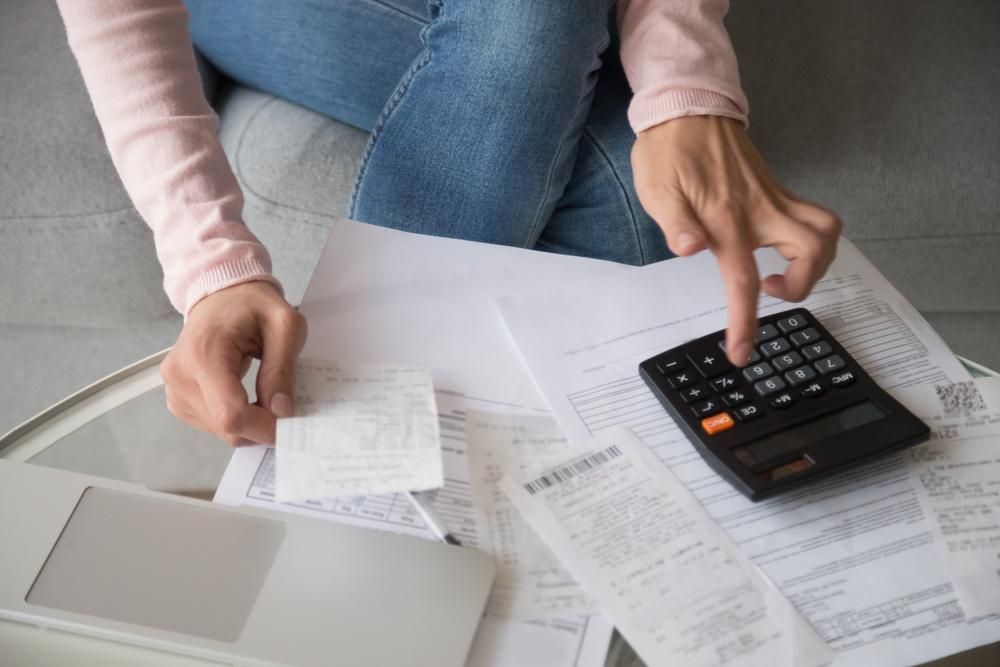 A Woman Is Sitting On A Couch Using A Calculator To Calculate Her Bills — NR Bookkeeping In Alstonville, NSW
