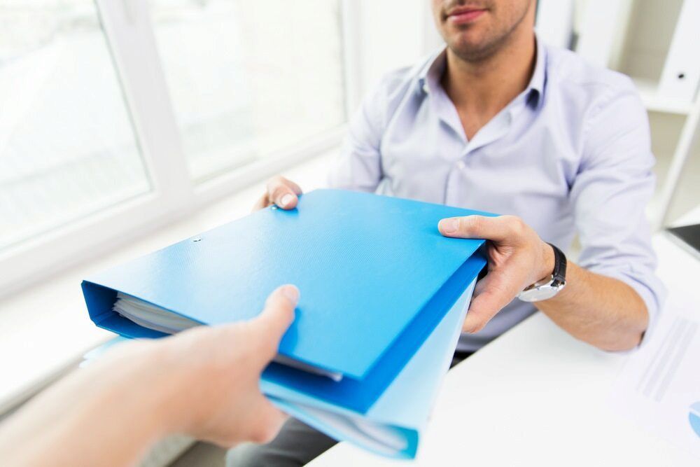 Hands Passing a Blue File Folder Over a Desk in an Office Setting — NR Bookkeeping in Lismore, NSW