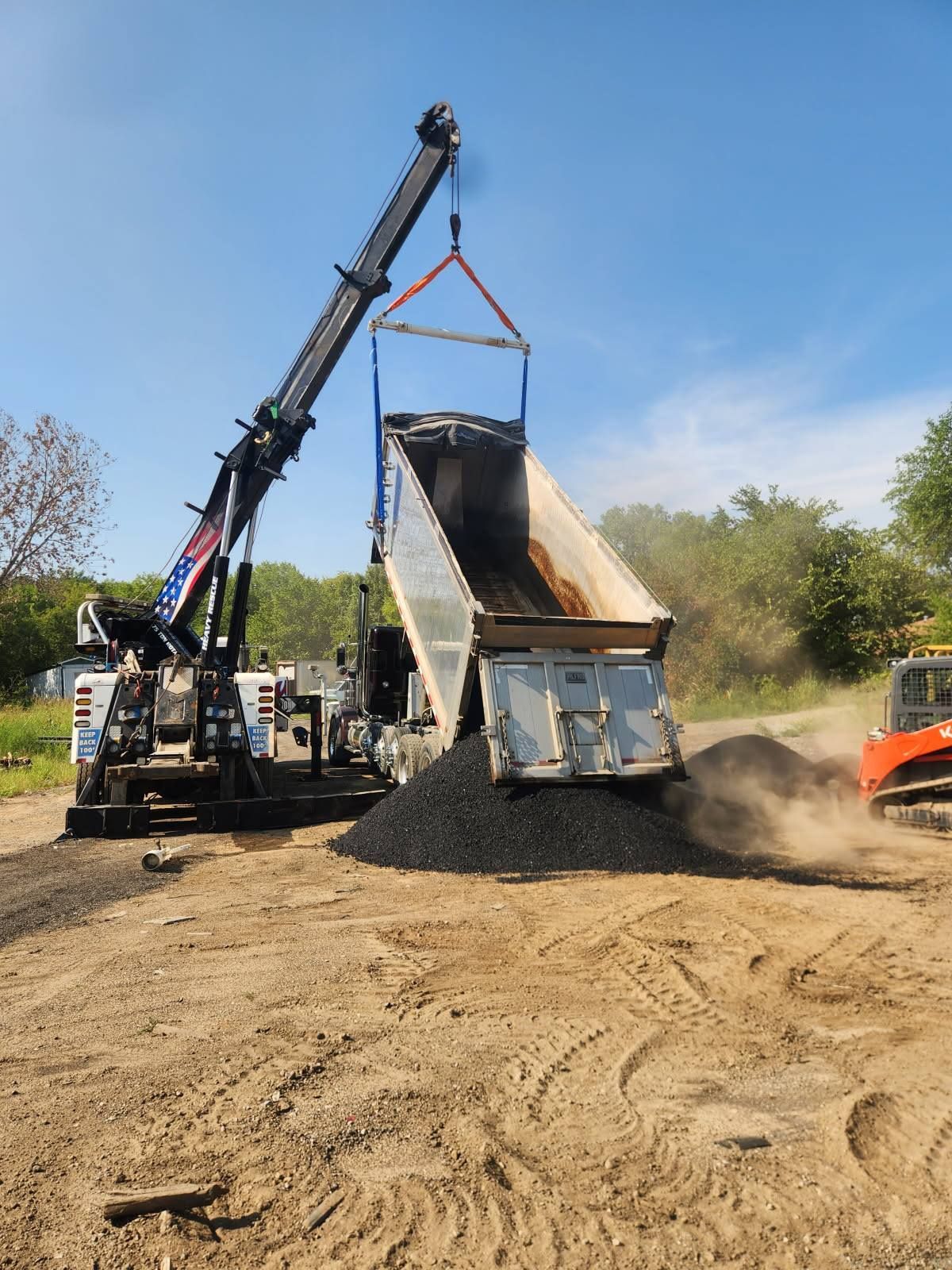 A dump truck is being loaded with dirt by a crane.